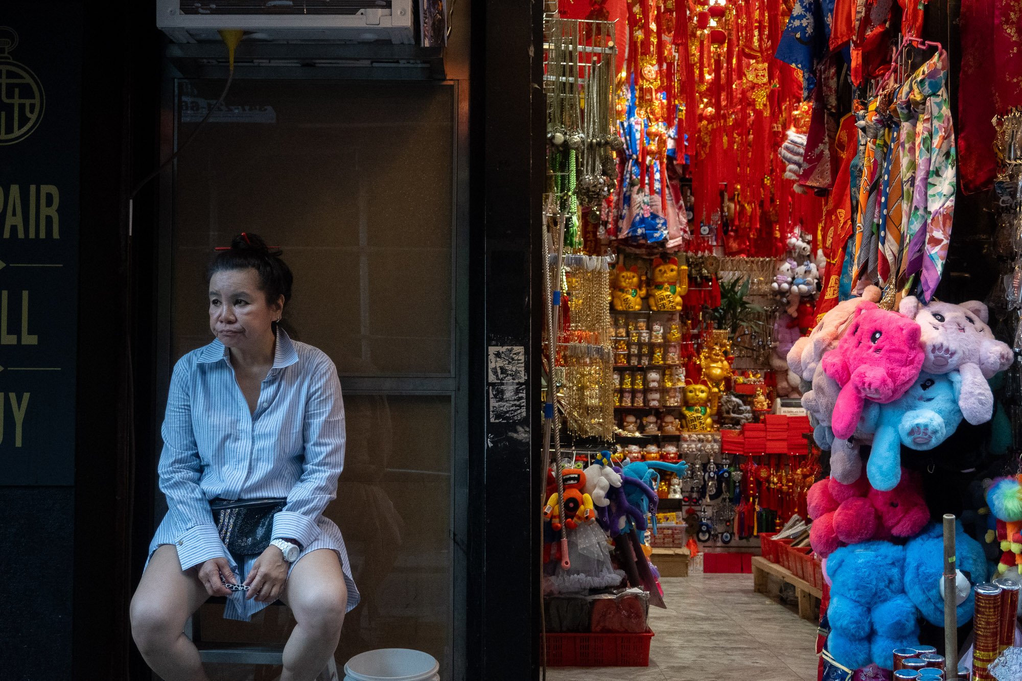 A woman in a blue and white striped shirt with black glasses on her head sitting outside a store with colorful plush toys and accessories on display.