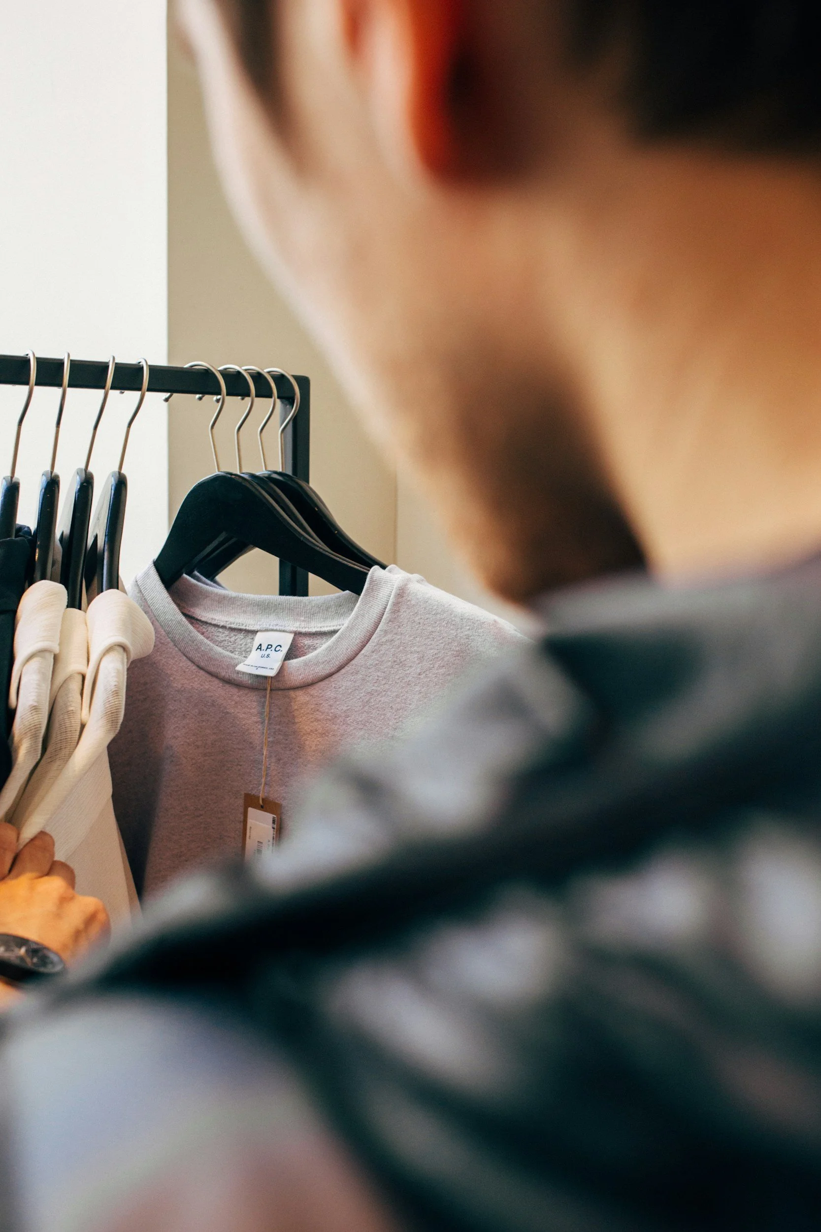 A person looking at a clothing rack with various garments, including beige and light pink. The person’s face is partially visible, and they appear to be inside a store.
