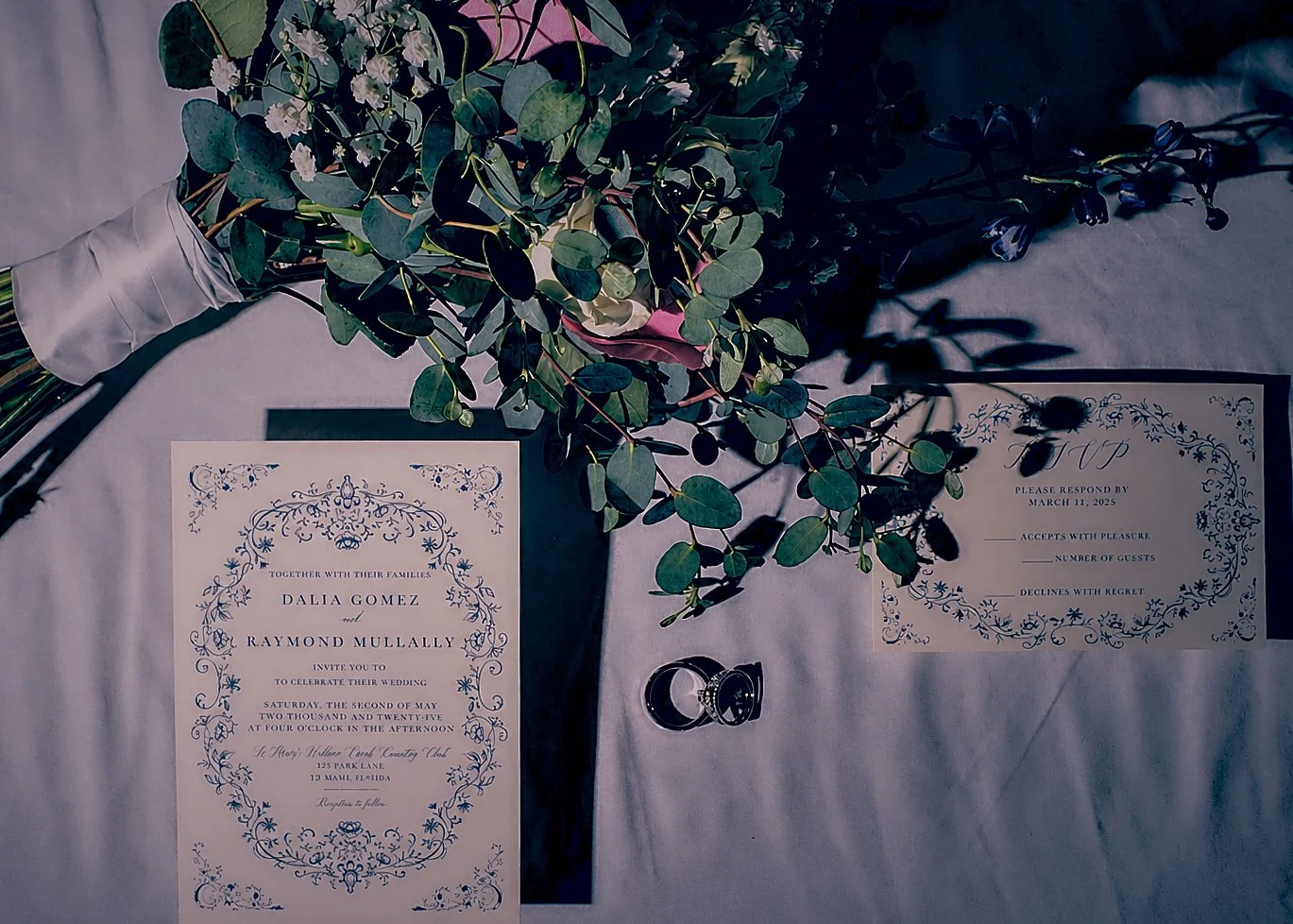 Wedding invitation, wedding rings, and a bouquet of eucalyptus on a table.
