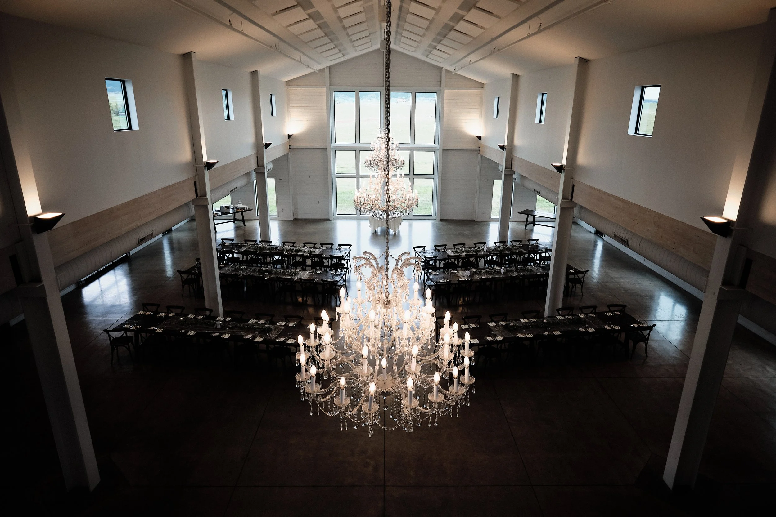 Elegant indoor event space with a large crystal chandelier hanging from a vaulted ceiling and multiple windows allowing natural light.