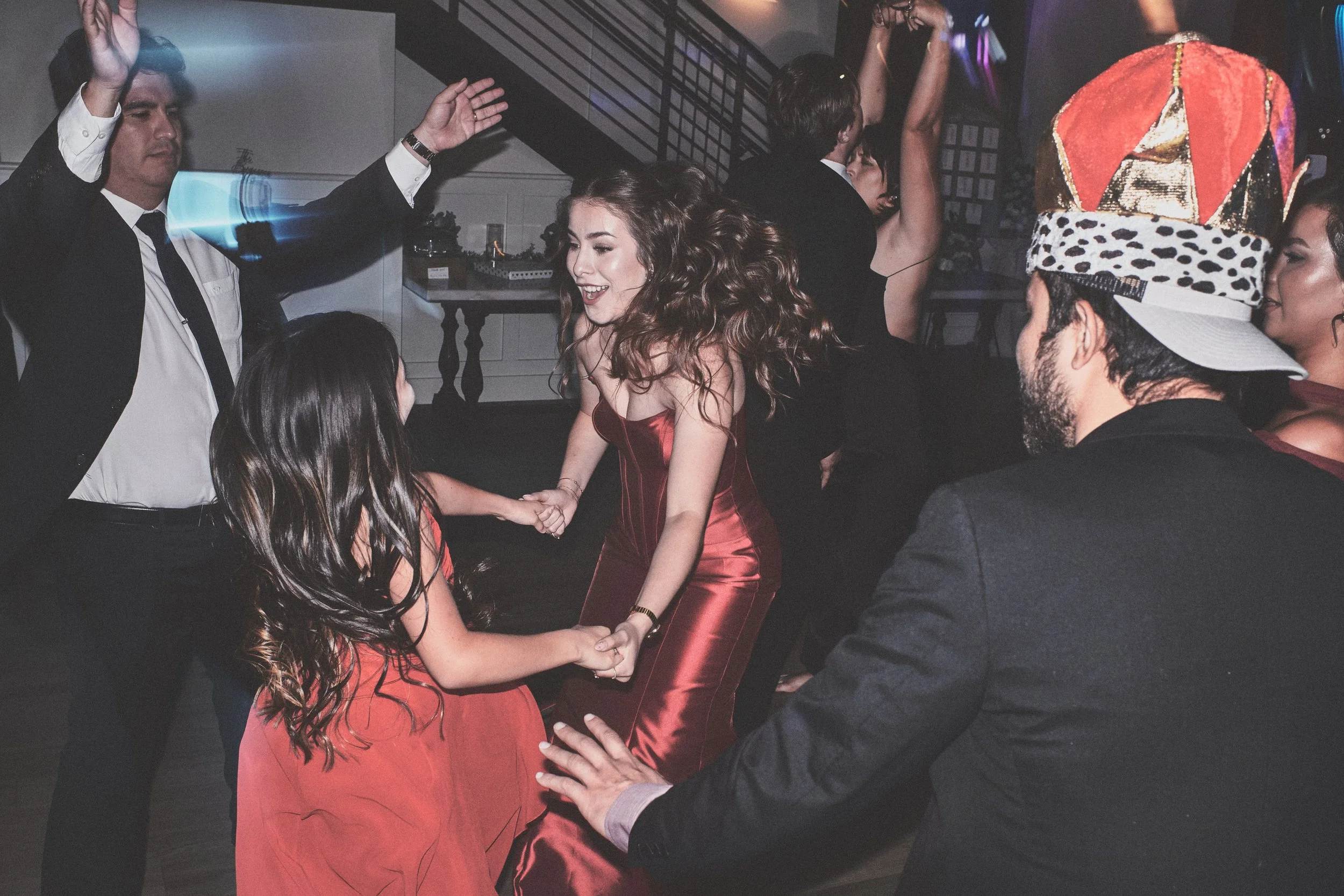 People dancing at a party, including a woman in a shiny red dress and a man in a black suit with a Festive hat.