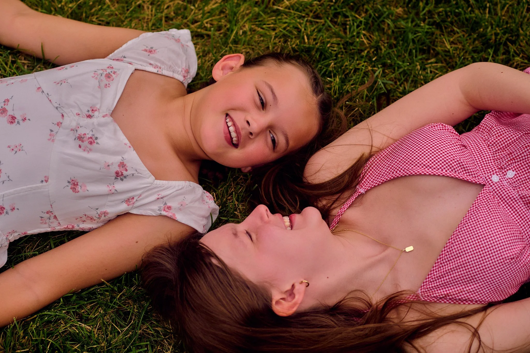 Three women lying on grass, smiling and relaxing outdoors.