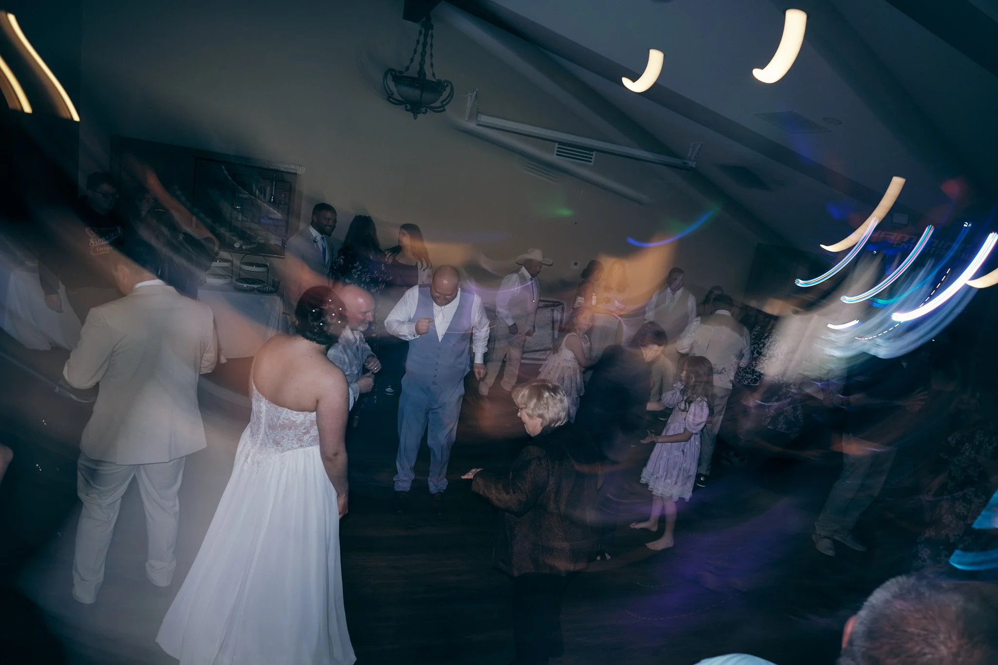 People dancing and socializing at an indoor party or wedding reception with colorful lights.