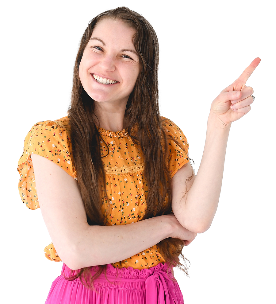 A woman with long brown hair, smiling and pointing to the right, wearing an orange floral blouse and pink skirt.