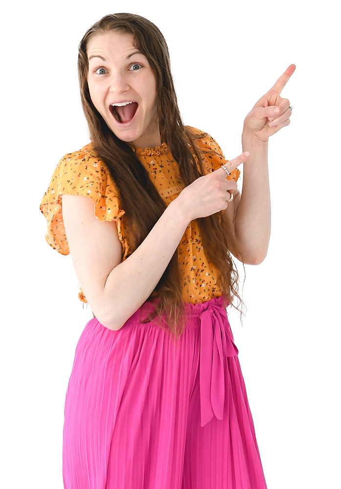 A woman with long brown hair, wearing an orange floral blouse and a pink pleated skirt, is smiling excitedly and pointing upwards with her right hand.