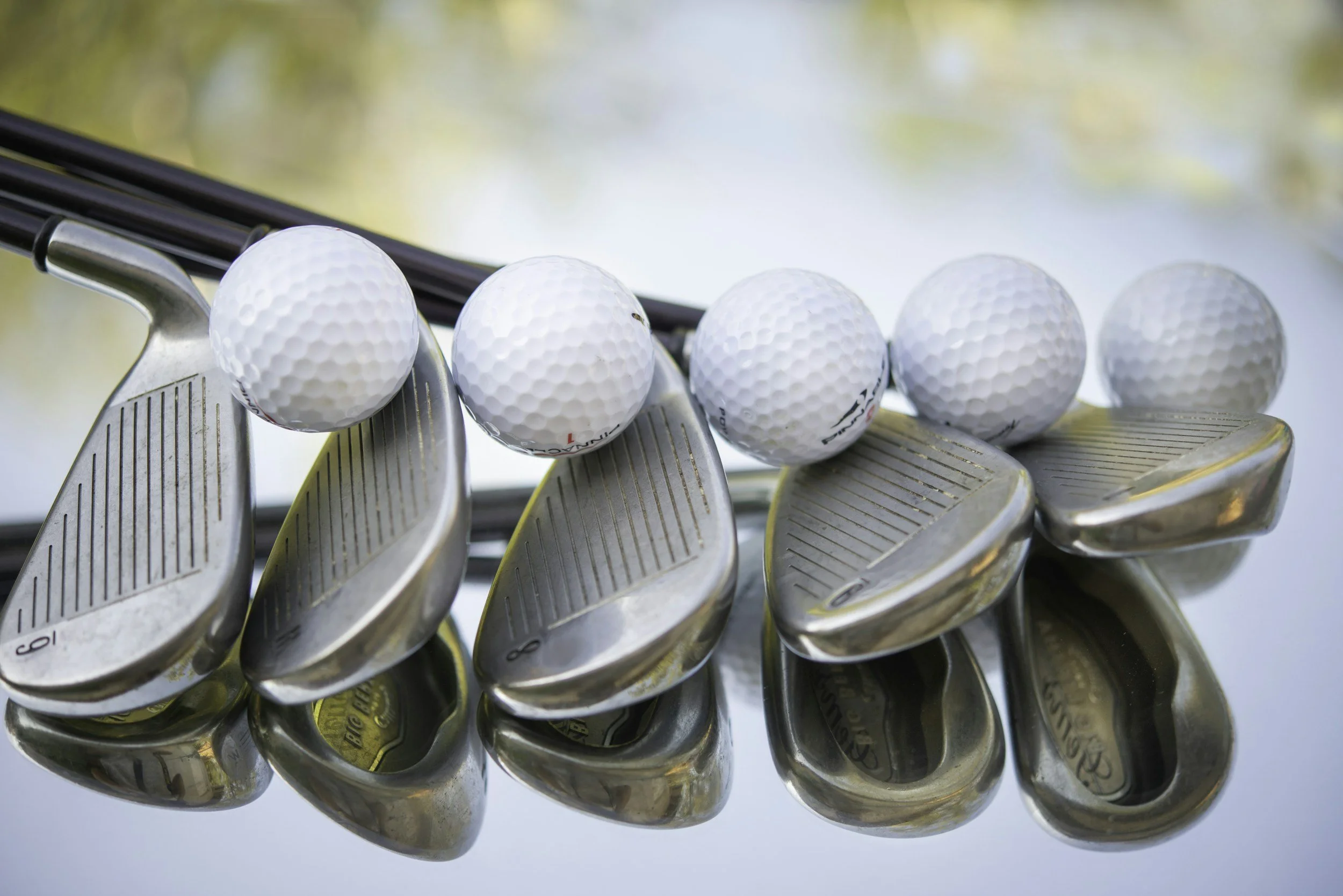 Close-up of golf clubs with golf balls resting on top, set against a blurred background.