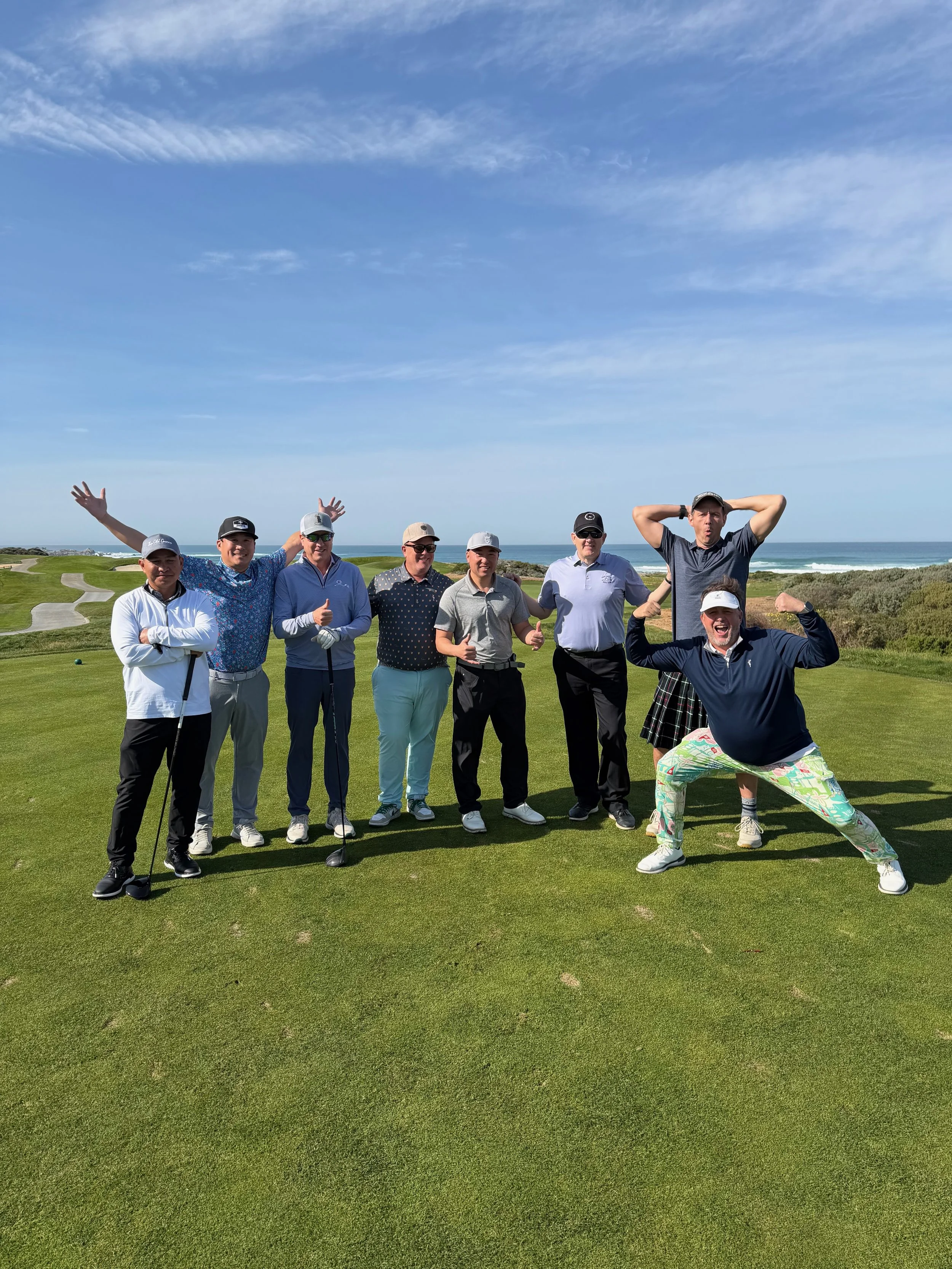 Group of nine people standing on a golf course near the ocean on a sunny day, striking playful poses. Spanish Bay, Monterey, California. Buddies golf trip.
