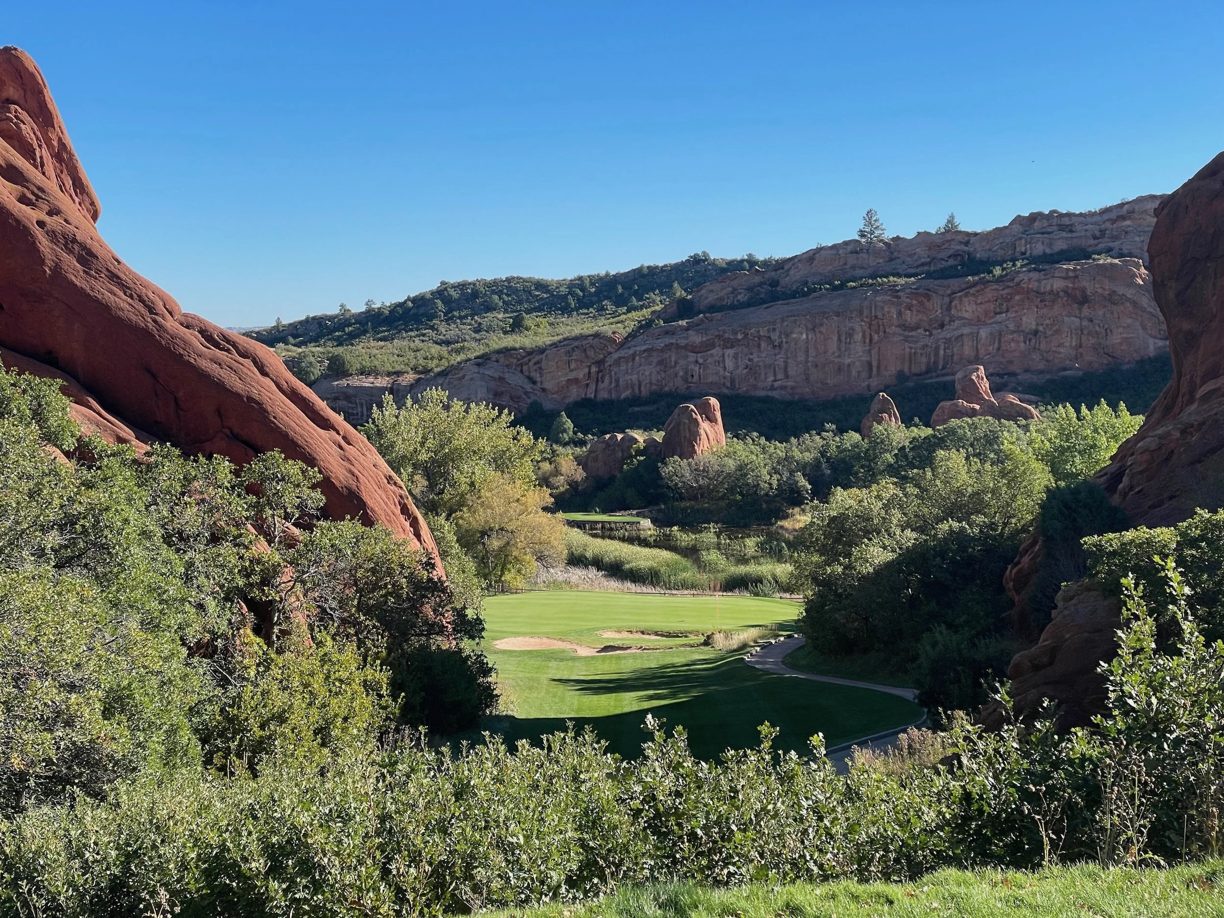 A scenic view of Arrowhead Golf Course in Colorado, surrounded by red-rock formations and green trees under a clear blue sky.