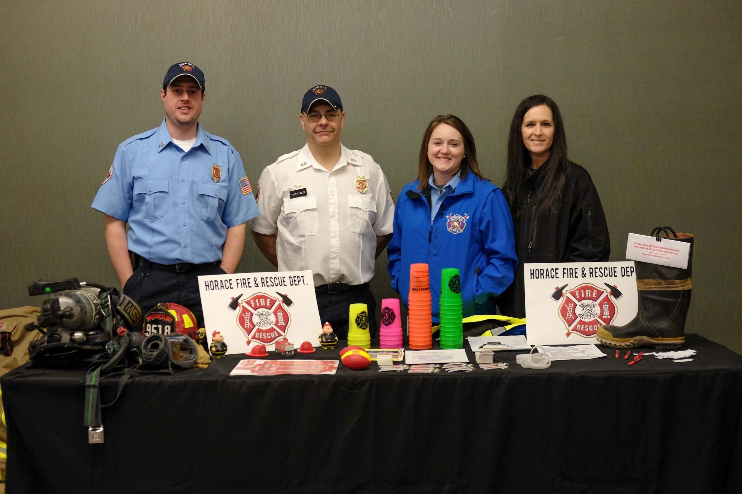 Group of four people standing behind a table displaying fire rescue equipment at the Horace Fire & Rescue Department event.