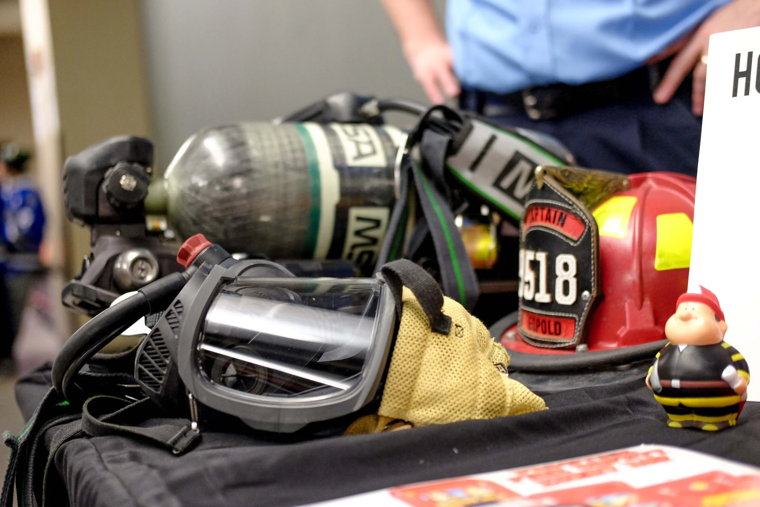 A collection of firefighter gear including a helmet, a breathing mask, gloves, and other equipment displayed on a table.