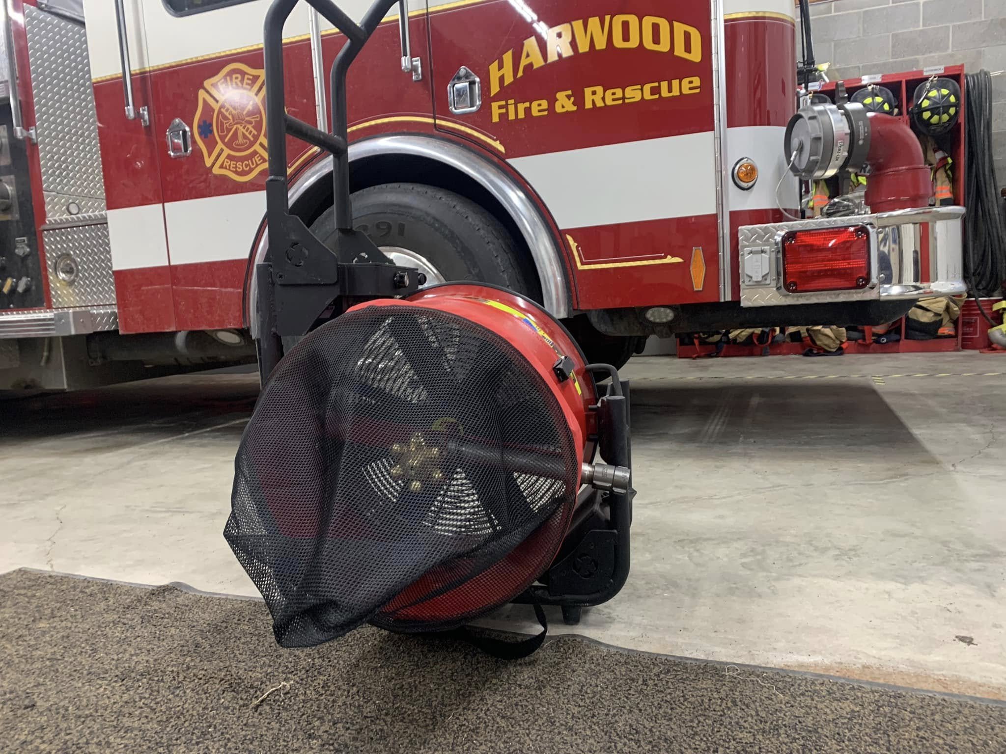 Close-up of a fire truck with the words 'Harwood Fire & Rescue' and the fire department emblem on it, a fire helmet, and firefighting equipment stored on the side.