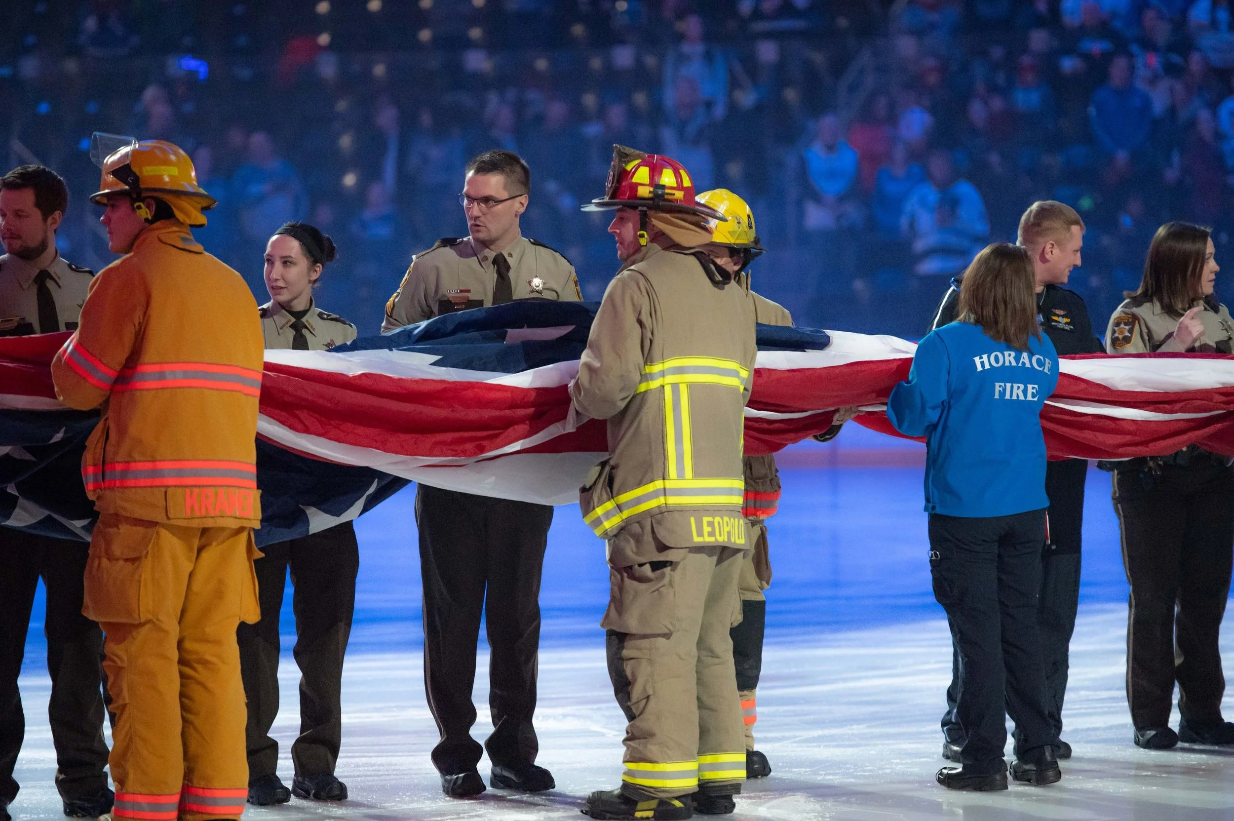 Firefighters and emergency personnel holding a large American flag on an ice rink.