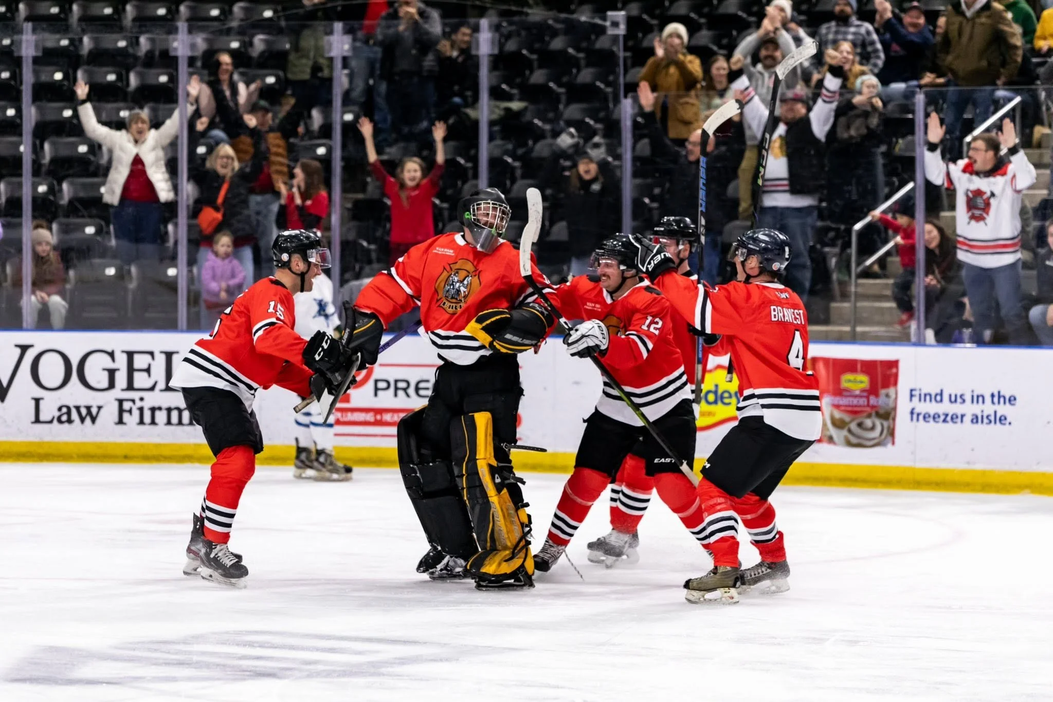 Hockey players in red jerseys celebrating on the ice rink while fans cheer in the stands behind a glass barrier.