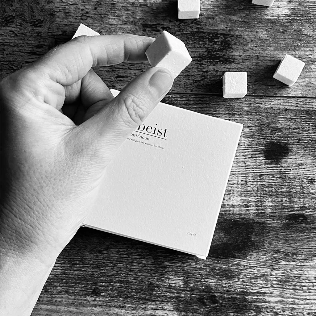 A hand holding a sugar cube above a white box labeled 'deist' on a wooden surface with additional sugar cubes nearby.