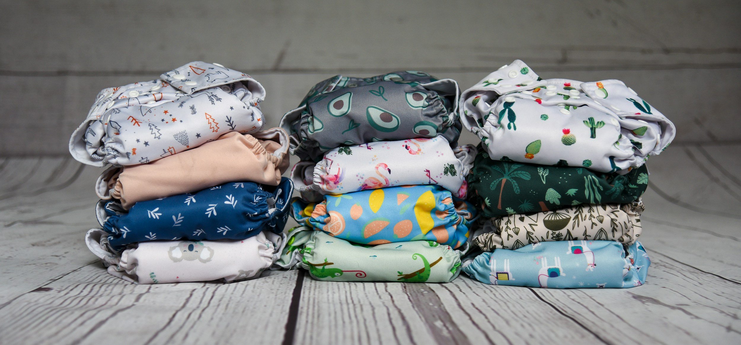 Stacks of folded cloth diapers with various colorful patterns on a wooden surface.