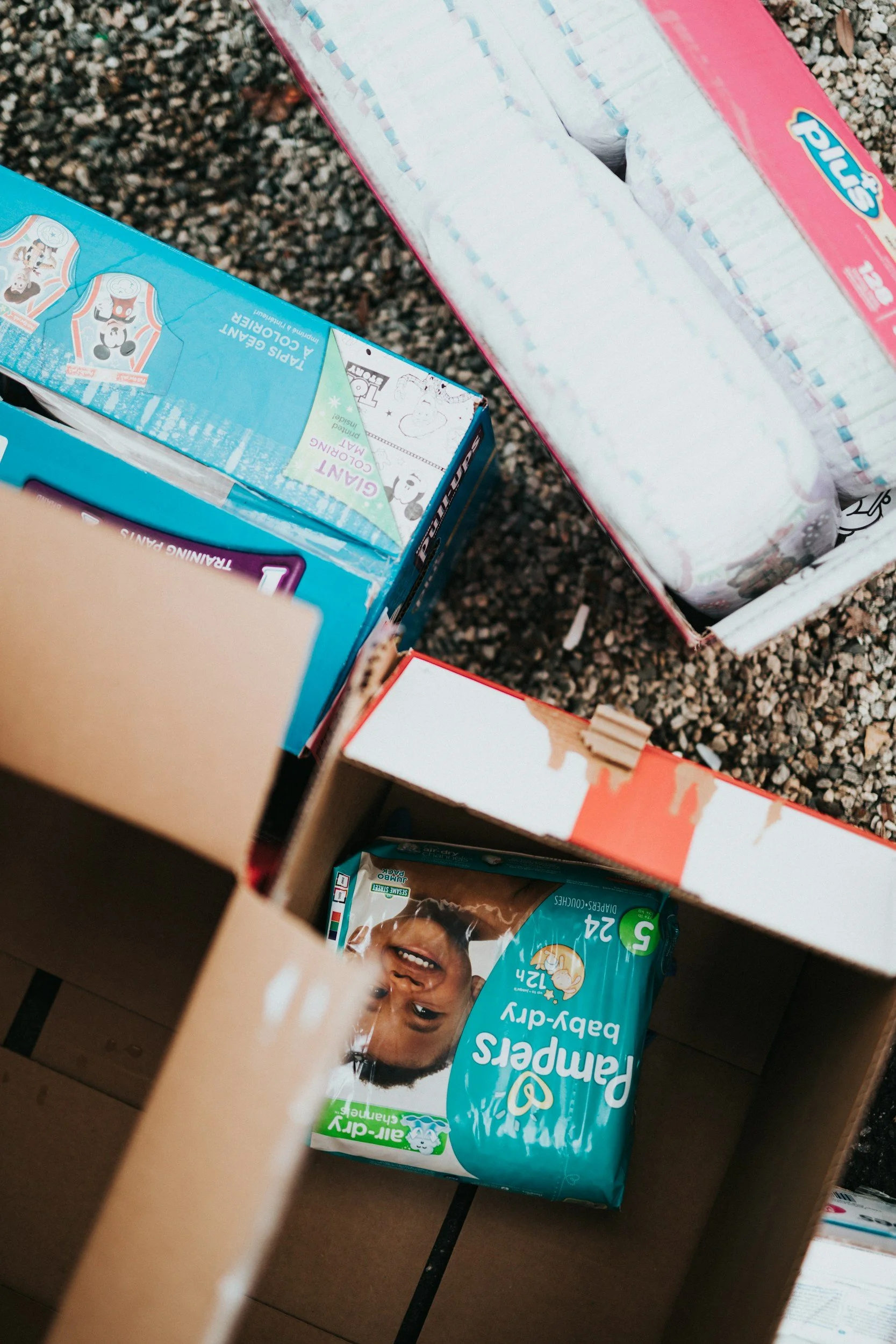 Open comic book storage box with various boxes inside, including a box of diapers with a child's photo, a package of diapers with a child's face, and a partially visible children's toy or snack package.
