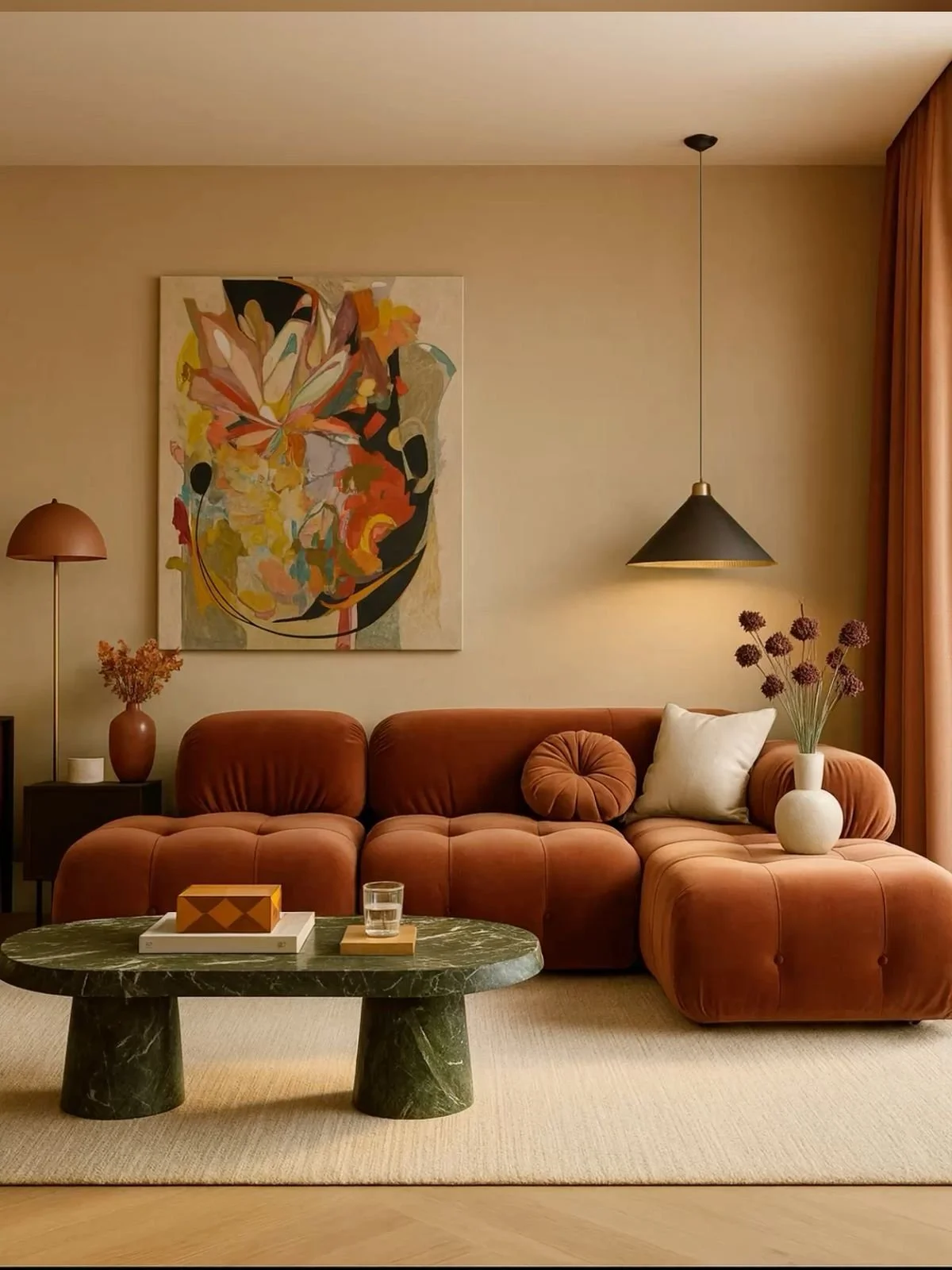 Living room with a rust-colored sofa, contemporary art painting, beige walls, black pendant light, floor lamp, vases with dried flowers, and a marble coffee table.