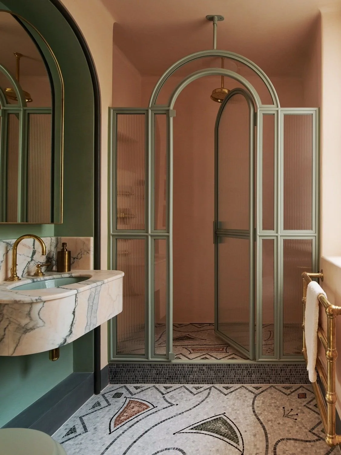 Luxurious bathroom with green accents, marble sink, gold fixtures, and a glass shower enclosure with arched design.