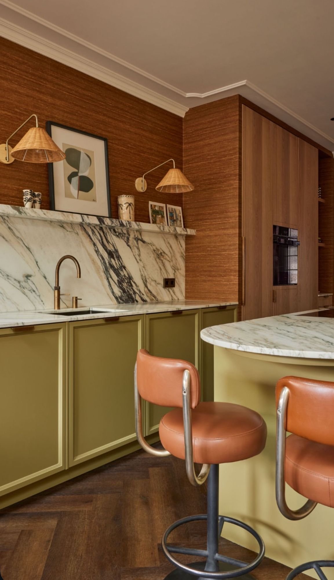 Modern kitchen with marble countertops, green cabinets, brown wood walls, and peach barstools.