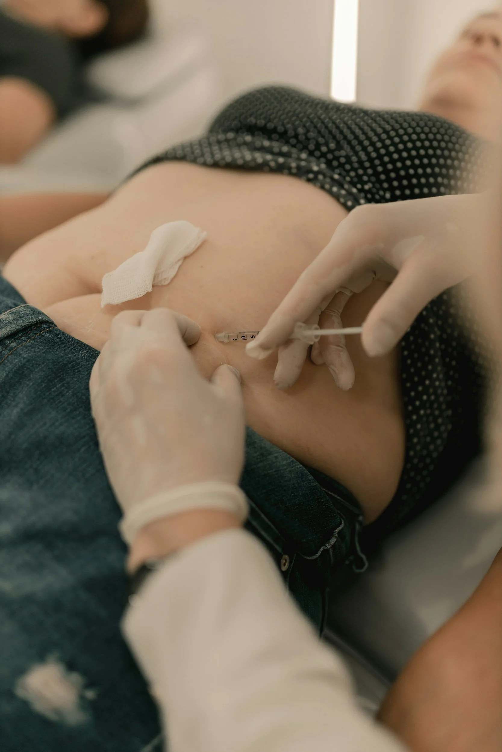A person receiving a vaccination shot in their upper arm by a healthcare professional wearing gloves.