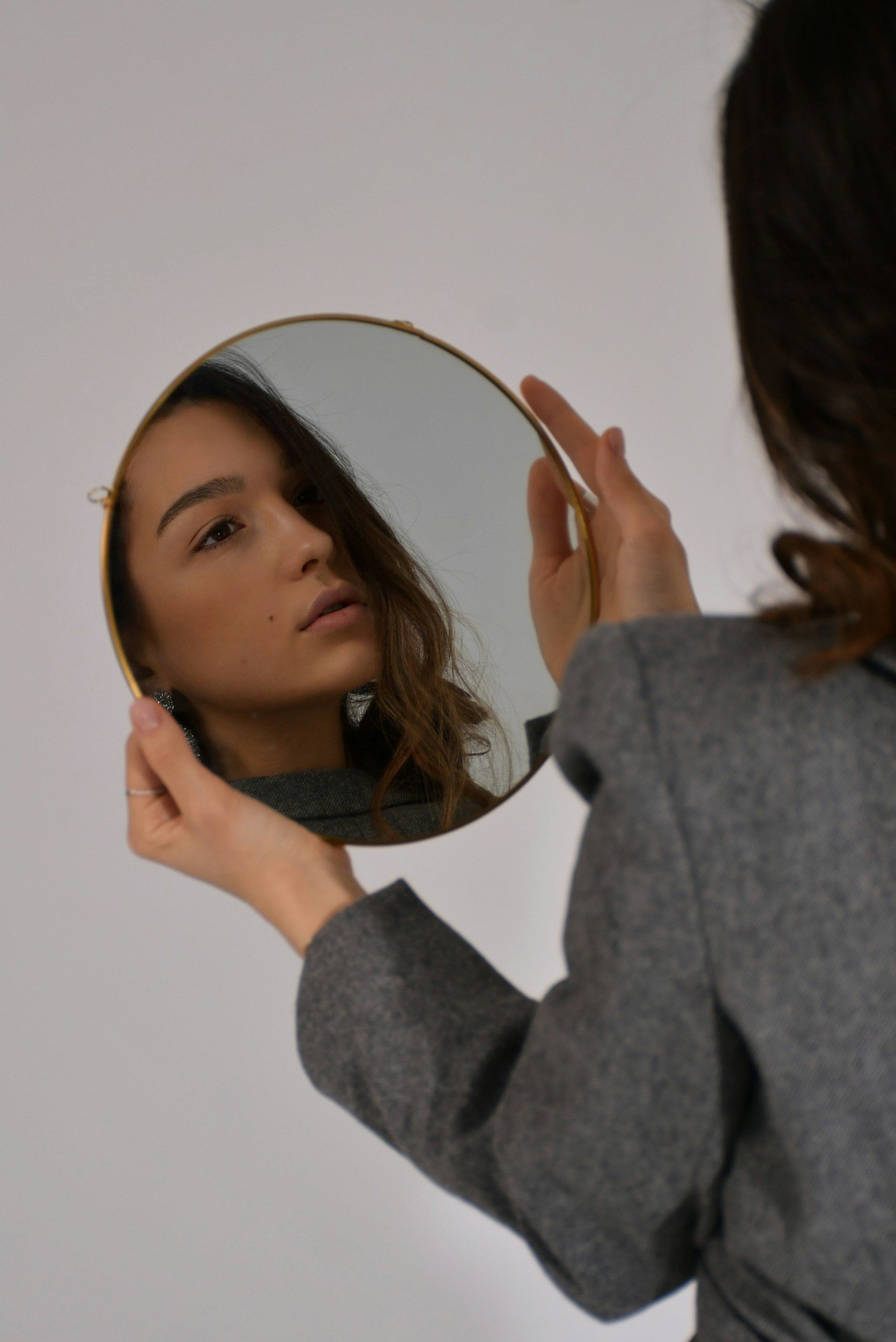 Person holding a small mirror, looking at their reflection, with a plain white background.