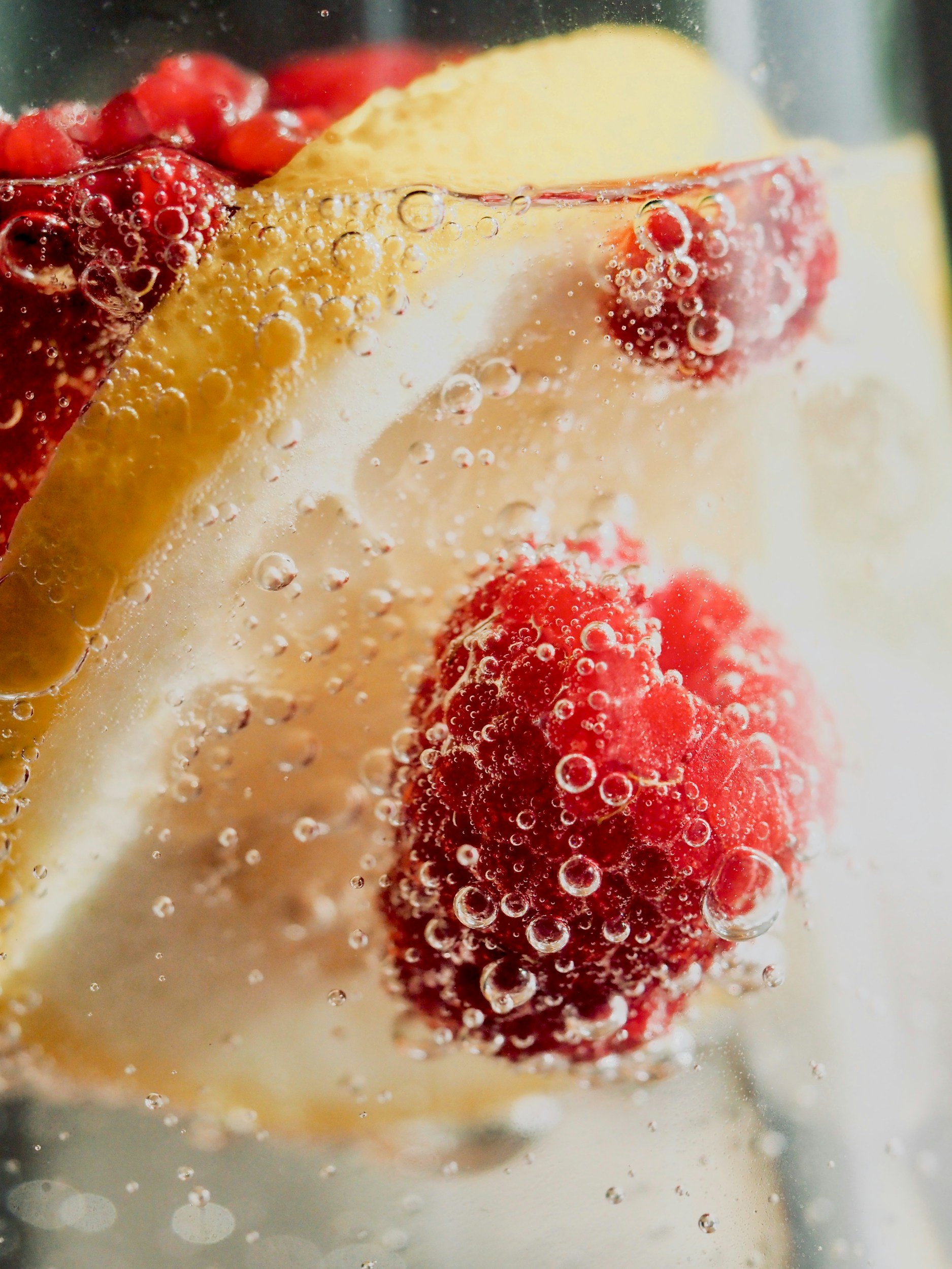 Close-up of strawberries and a lemon slice submerged in sparkling water with bubbles