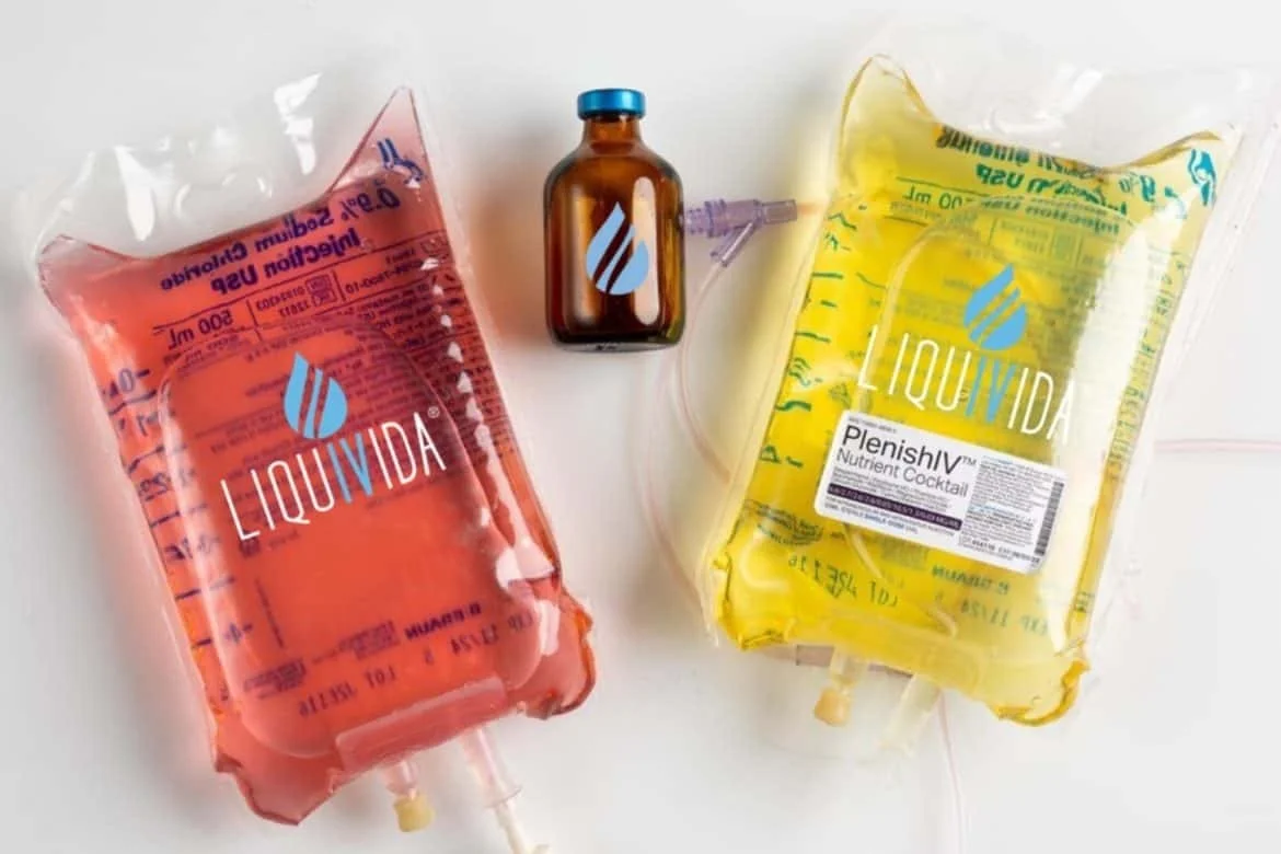 Two IV fluid bags, one with red liquid labeled "Liquivida" and one with yellow liquid labeled "Plenish"; a small brown medicine bottle with a blue cap and connected IV tubing.