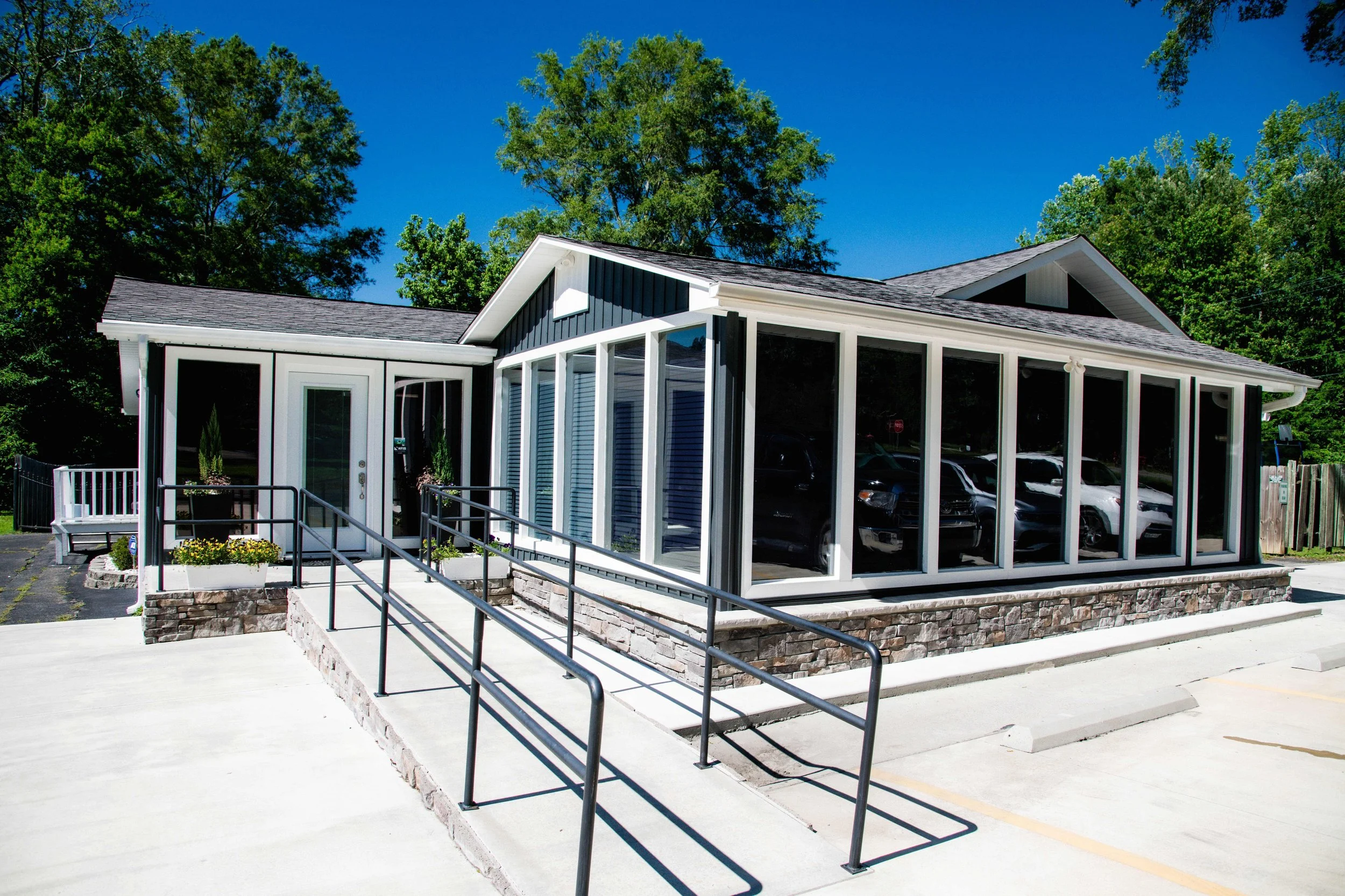 A building with large windows and a porch, surrounded by trees, with parking spaces in front and a clear blue sky.