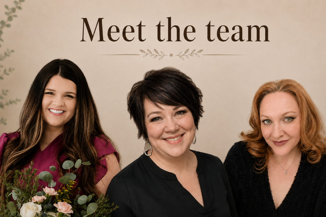 Three women smiling in front of a "Meet the team" sign, with one holding a bouquet of flowers.