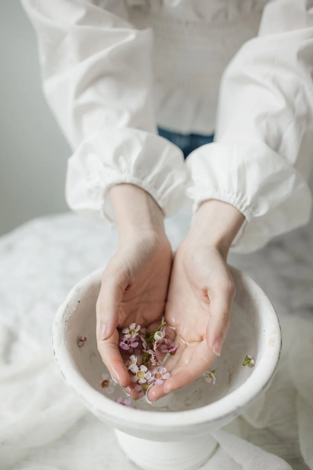 Person wearing a white long-sleeve shirt holding pink and white flowers in a white bowl.