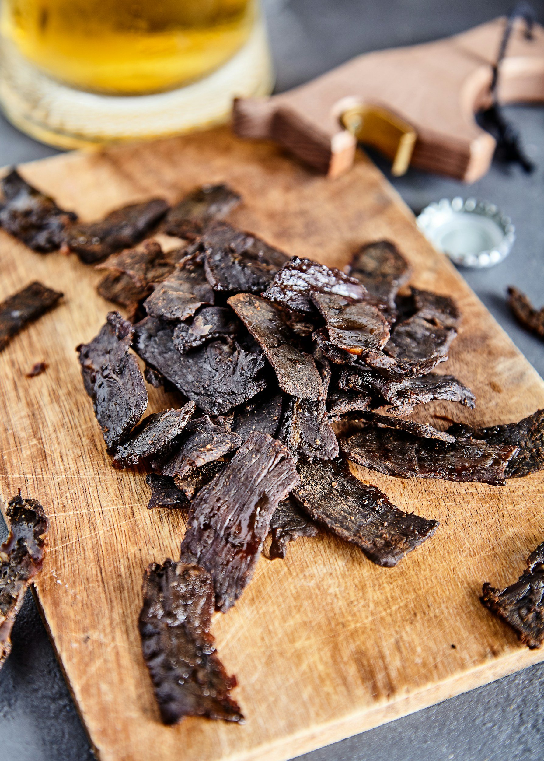 Sliced beef jerky on a wooden cutting board, with a jar of honey and a wooden honey dipper in the background.