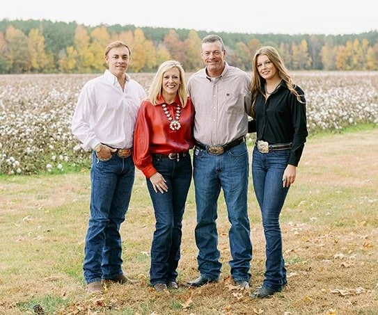 A family of four standing outdoors in a cotton field, smiling and posing for the camera.