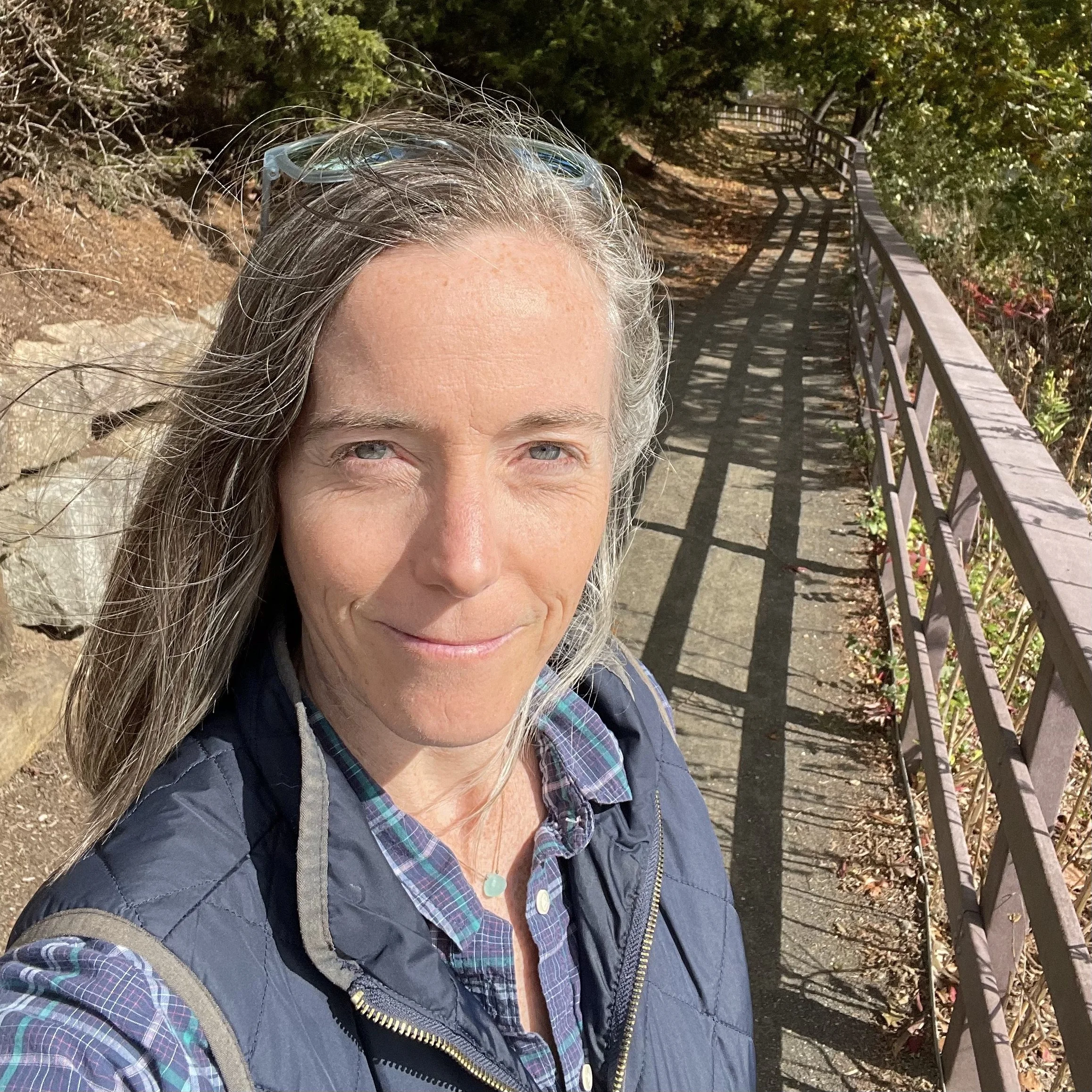 Mary VonO standing beside a wooded path, looking toward the camera
