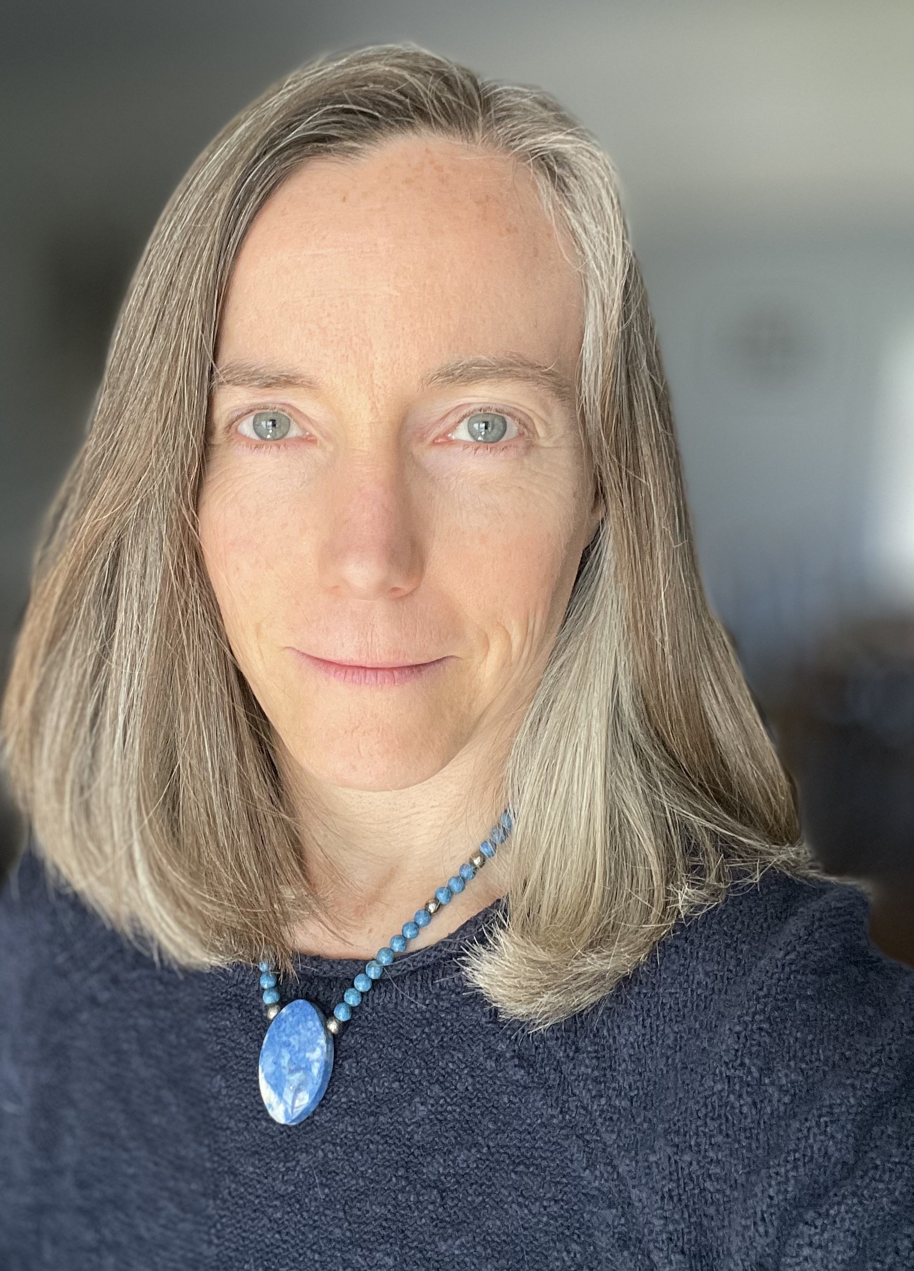 Mary VonO looking at the camera in a close-up portrait, wearing a blue stone necklace