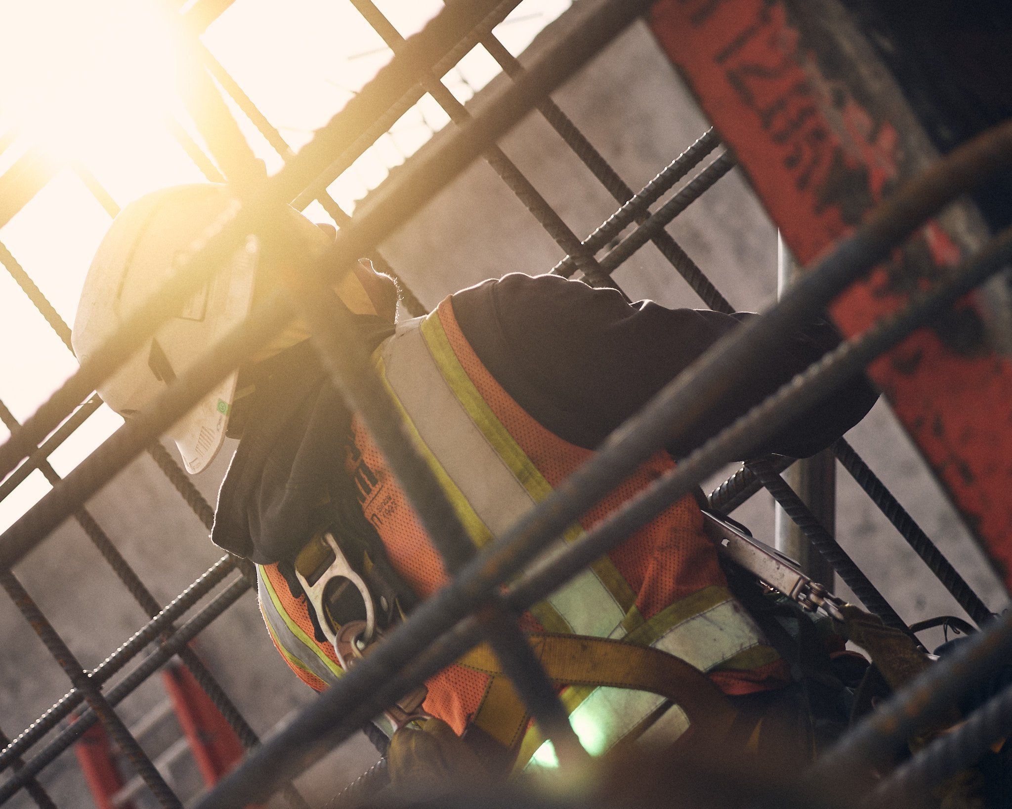 A person wearing a reflective safety vest and gloves, working behind metal bars, with a bright light shining from the top left.