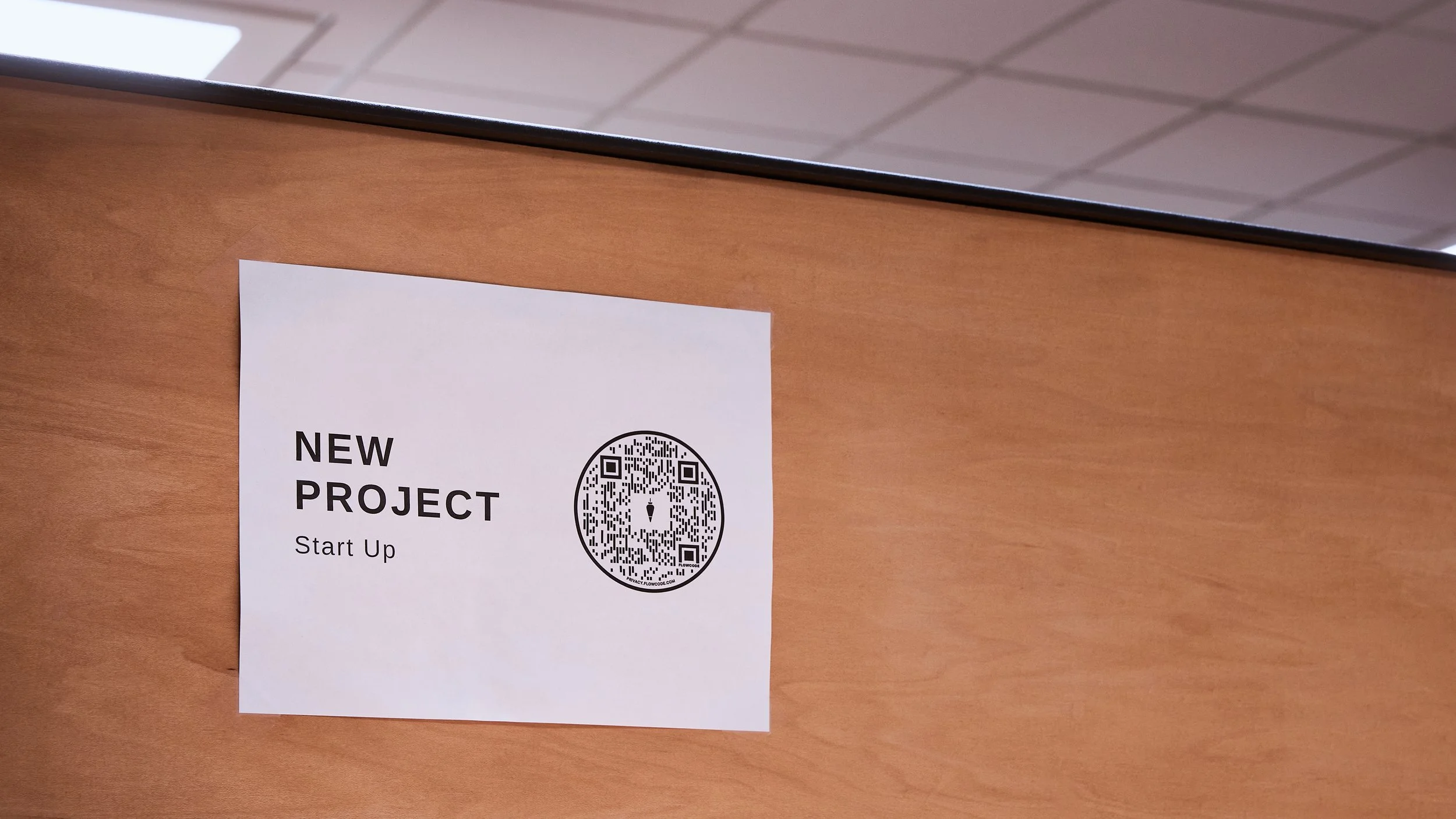 A printed flyer on a wooden surface advertising a new project for start-up, featuring a QR code.
