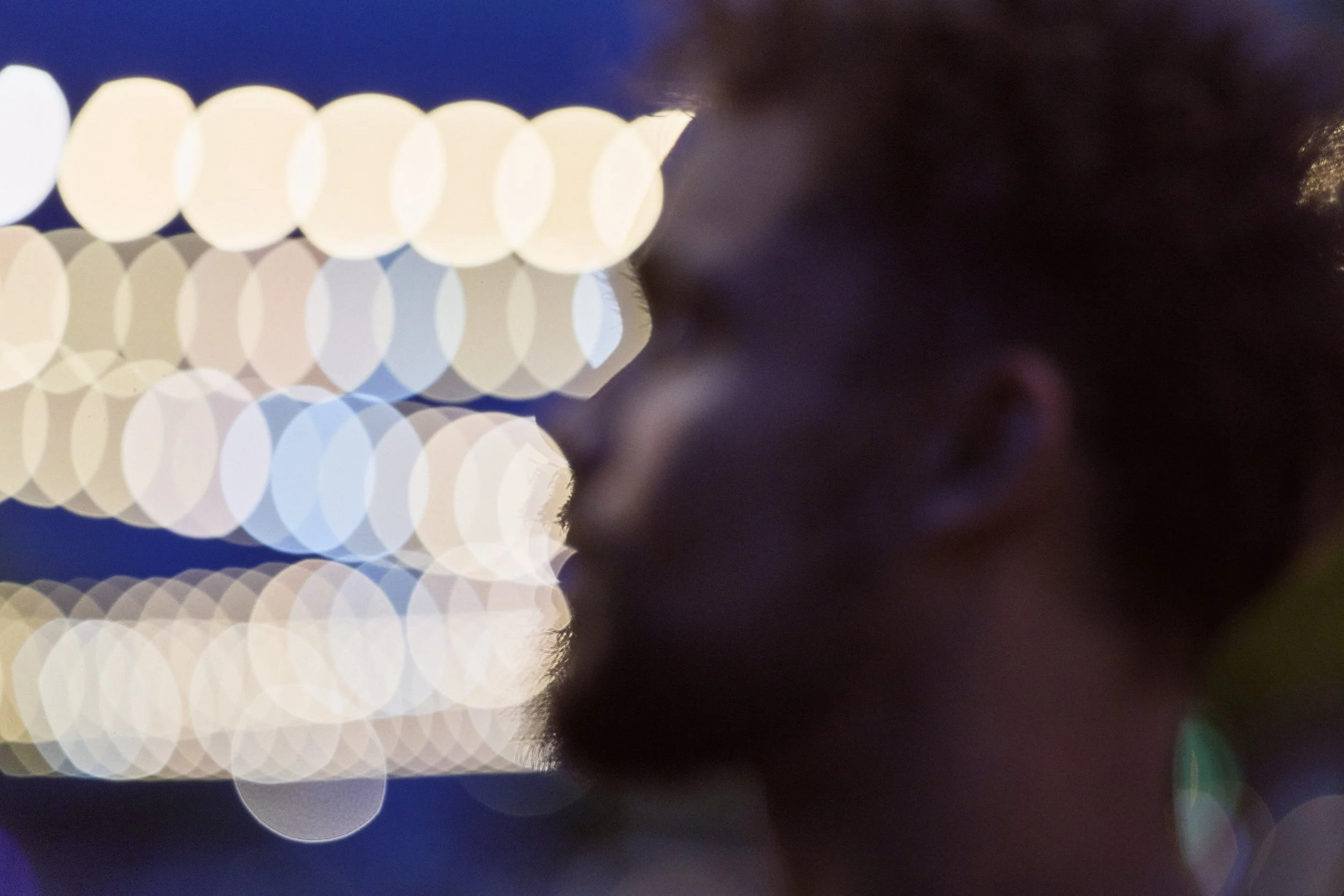 Close-up image capturing blurred circular bokeh lights with dark and purplish background, possibly on a reflective surface.