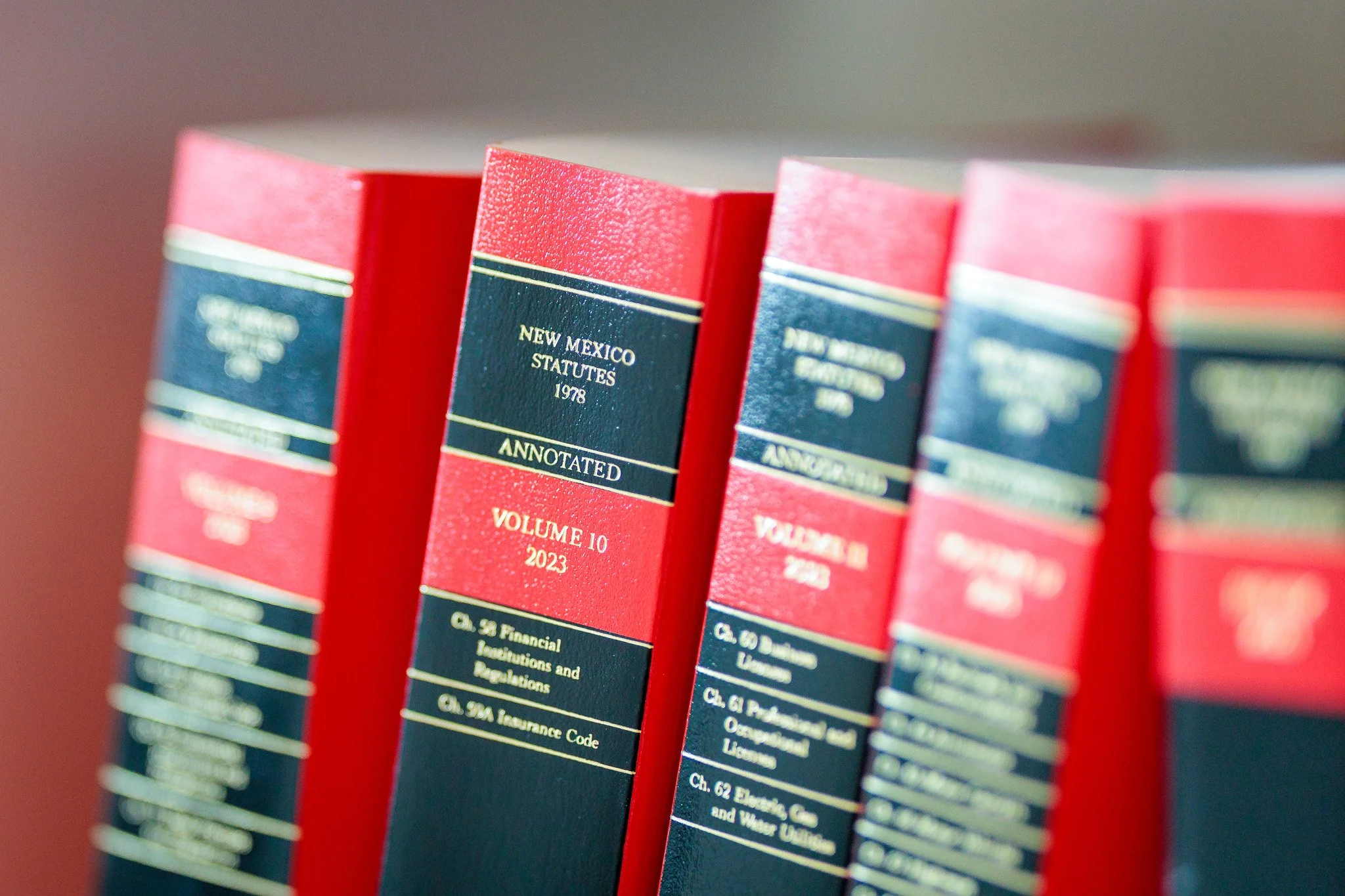 Close-up of several red books titled 'New Mexico Statutes 1978' with additional text indicating they are annotated and volume 10, 2023, standing upright on a shelf.