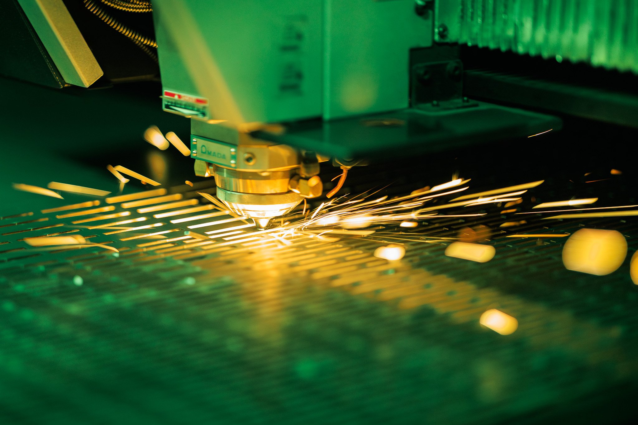 A laser cutting machine processing metal, with sparks flying as laser cuts through material under greenish lighting.