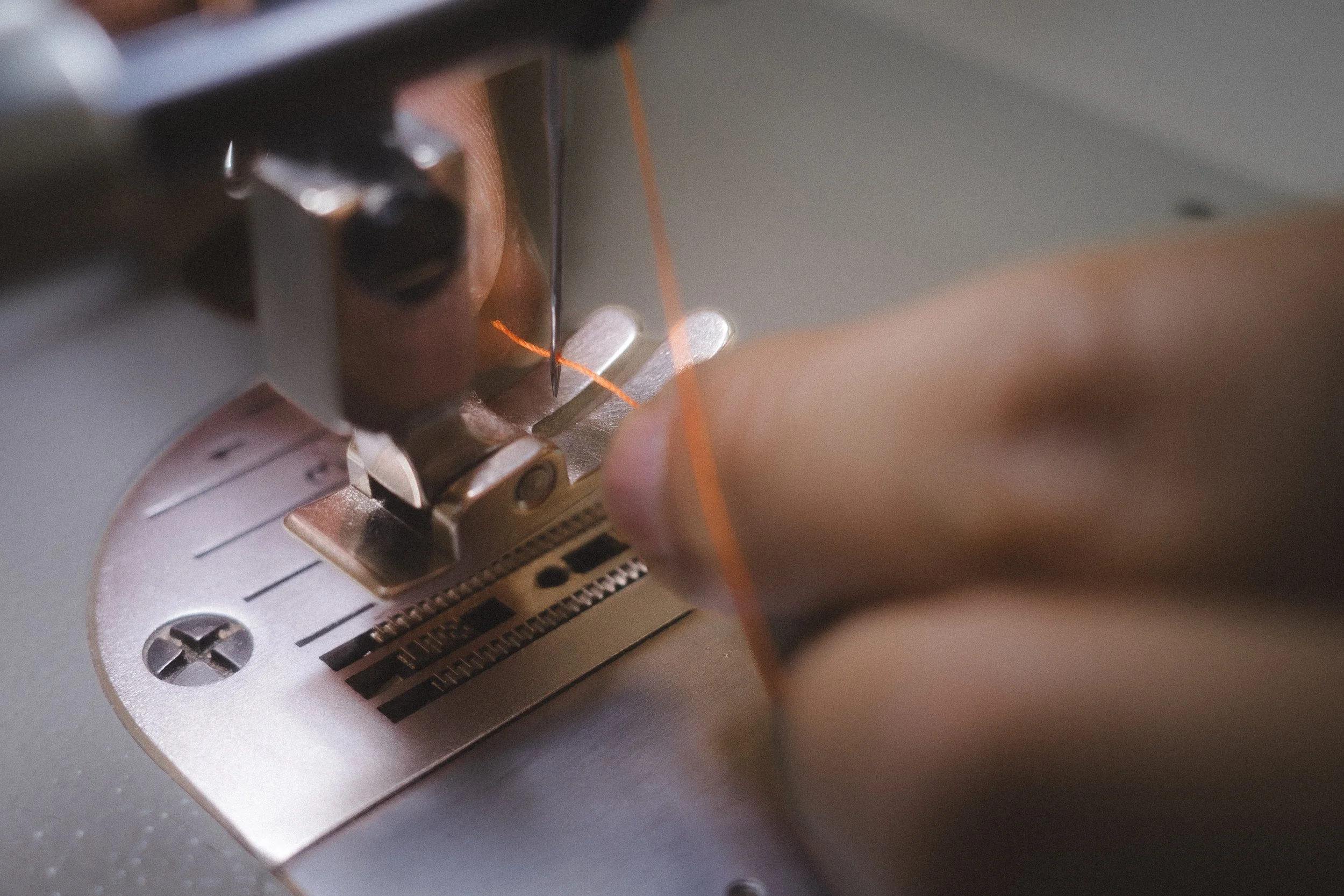 Close-up of a sewing machine needle sewing orange thread through fabric on a metal plate with measurement markings.