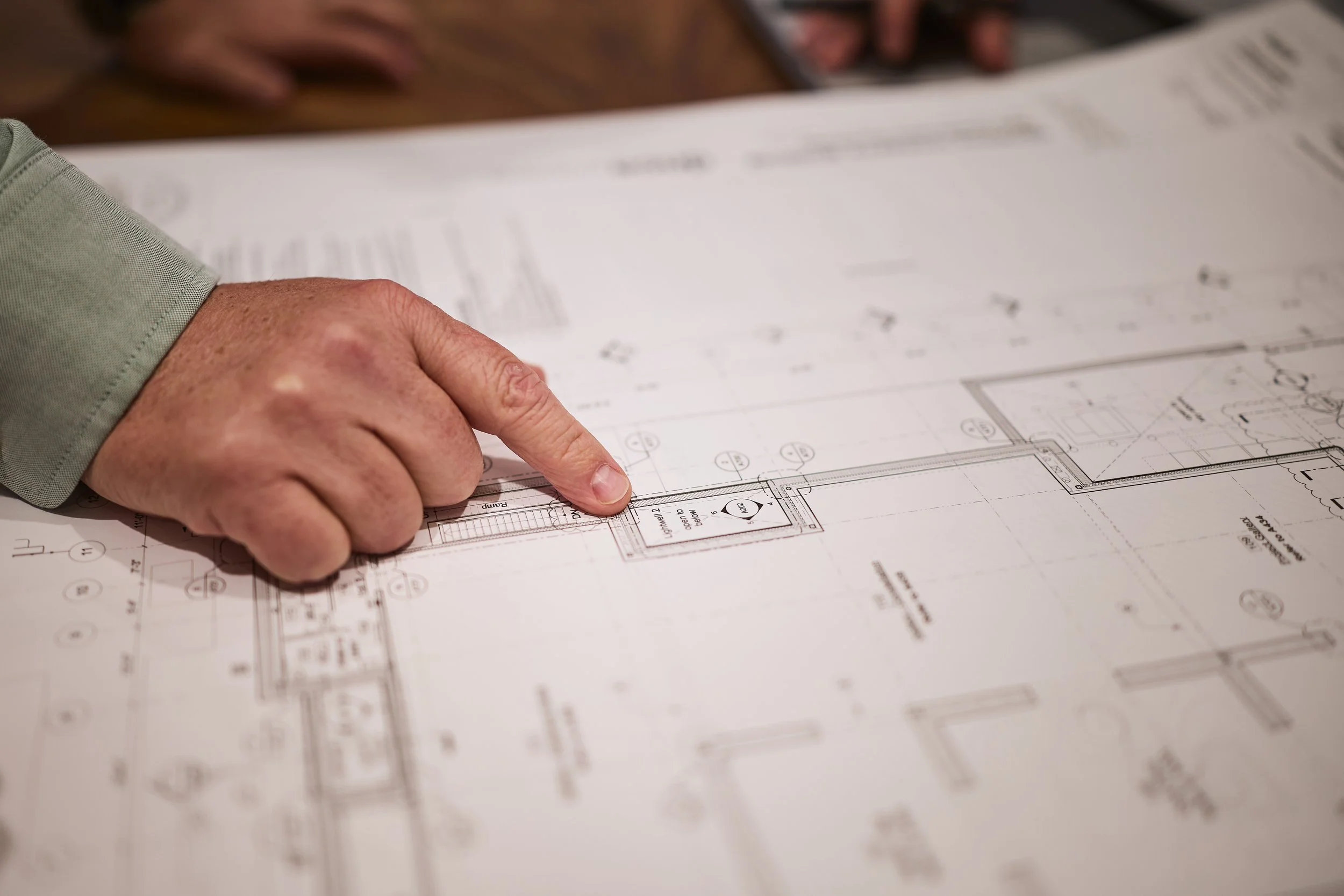 A person pointing at a detailed architectural blueprint on a table.