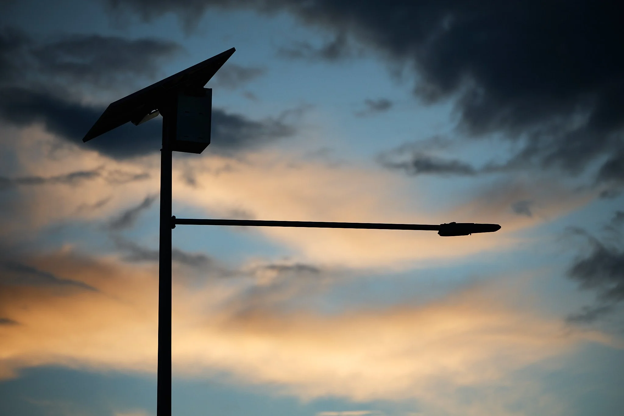 Silhouette of a solar panel structure against a cloudy sky at dusk or dawn.