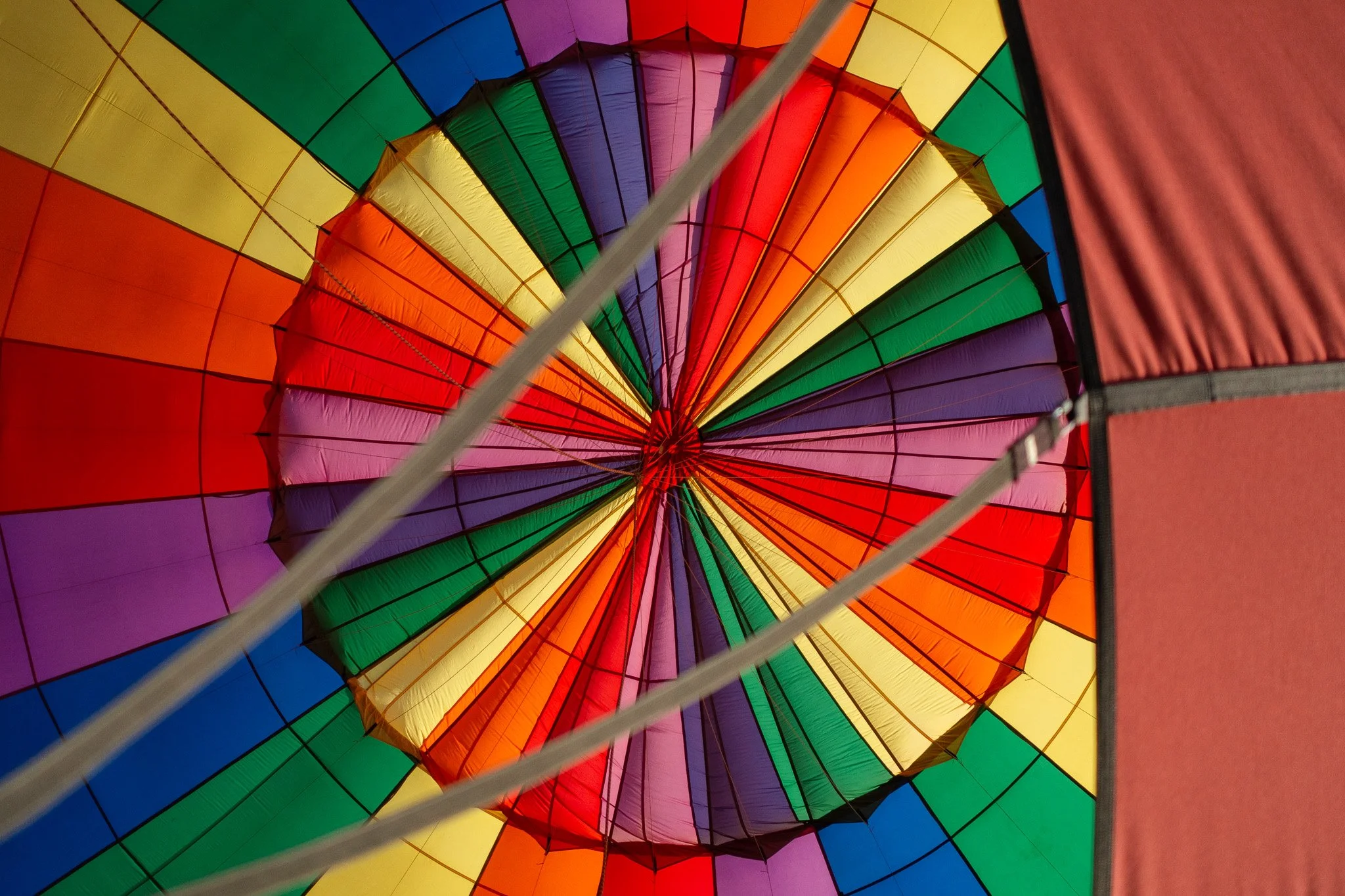 Inside view of a colorful hot air balloon with a rainbow pattern, showing the fabric panels and the central support rod.