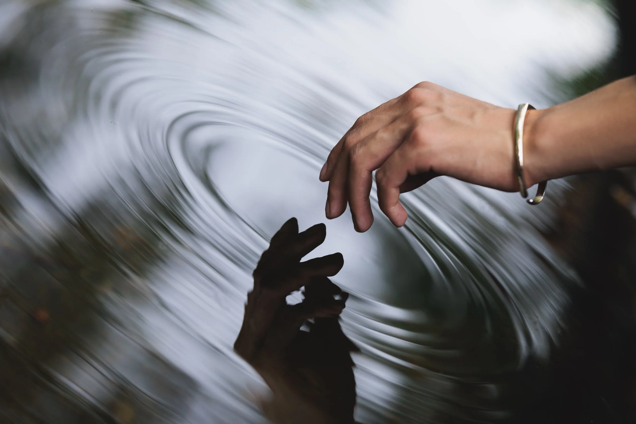 Close-up of a person's hand touching water with a ripple effect.