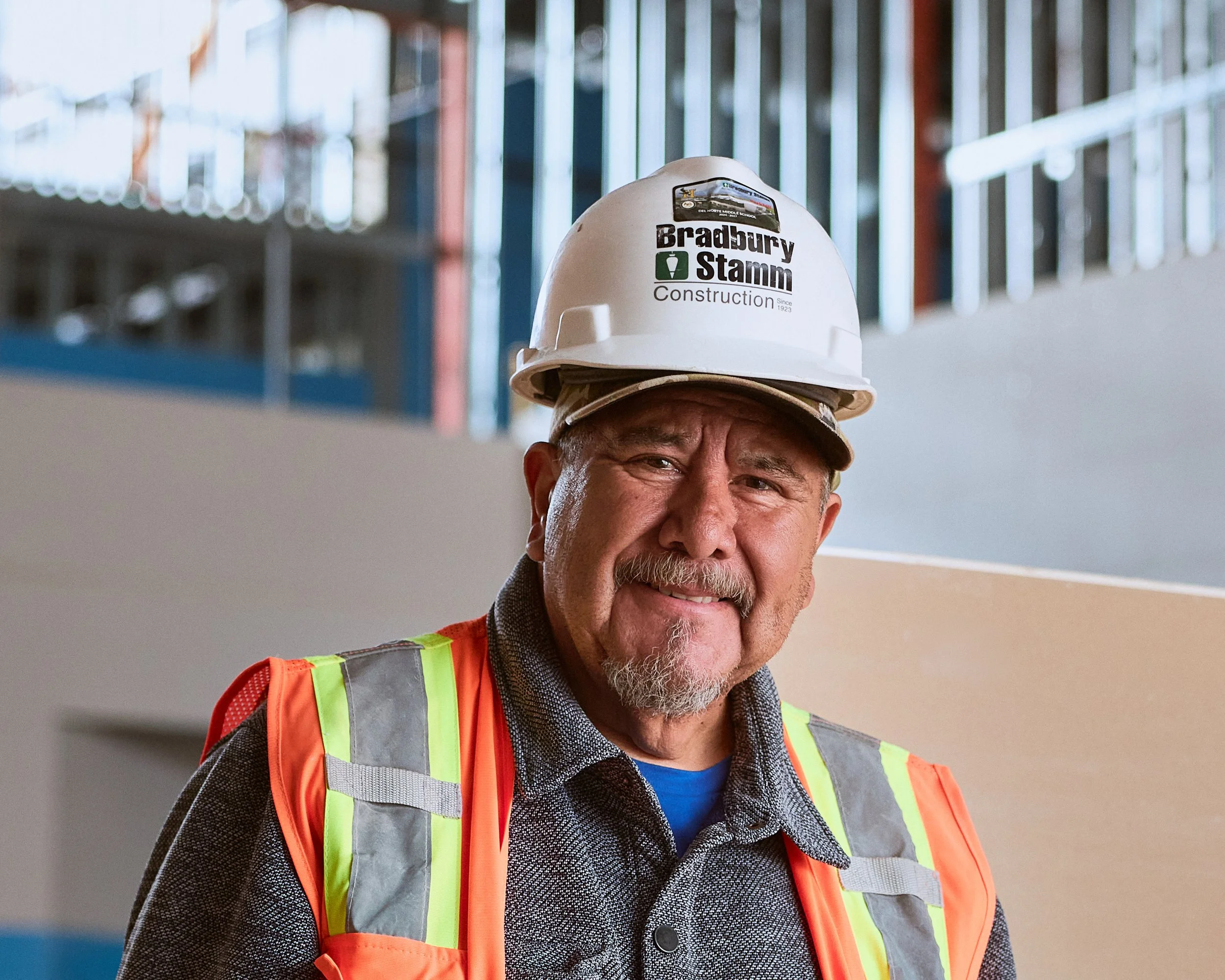 Close-up of an older man wearing a construction helmet and a high-visibility safety vest at a construction site.