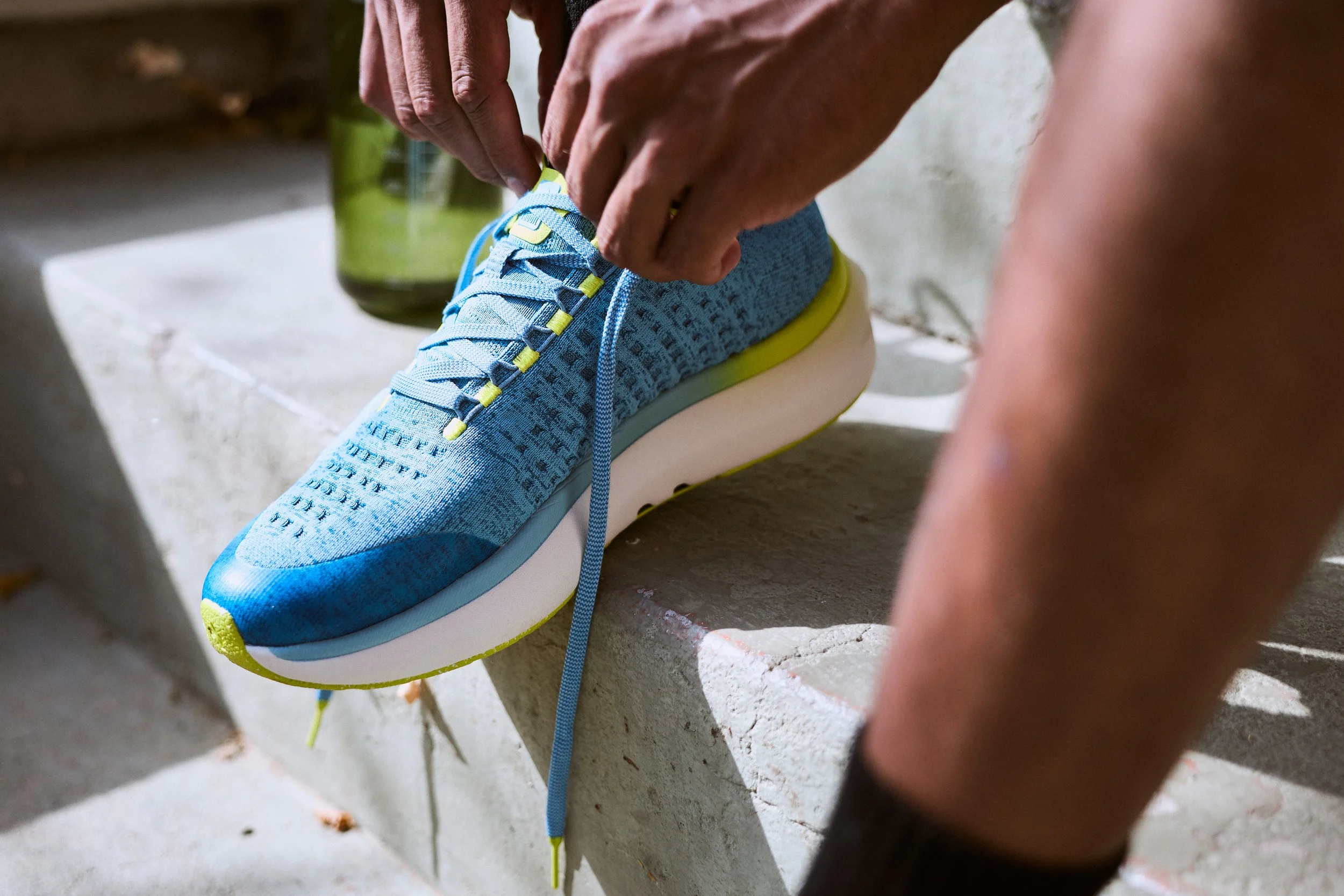 A person tying the shoelaces of a blue sneaker with yellow accents.