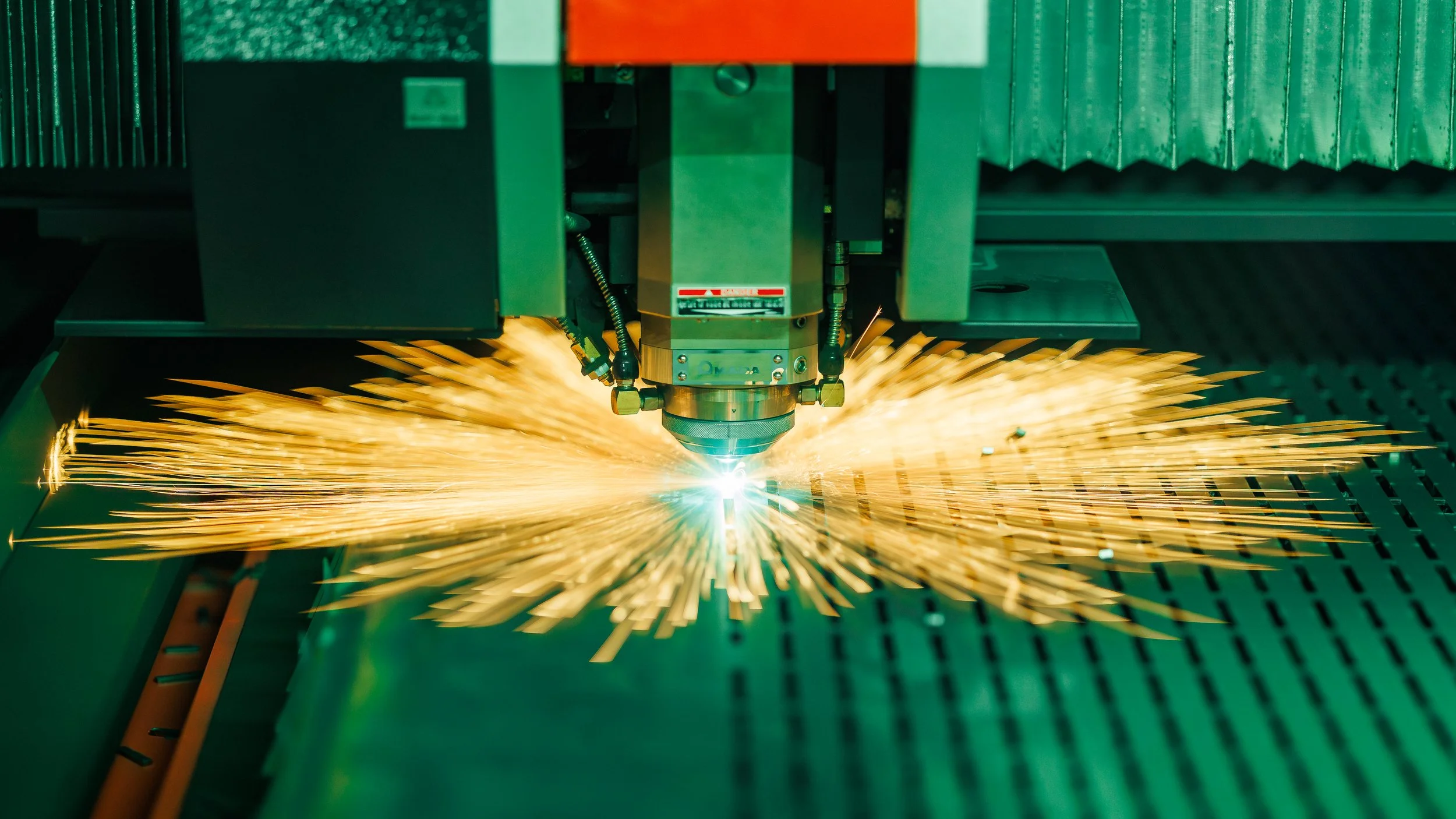 A laser cutting machine cutting through metal, producing bright sparks and a bright blue laser beam at the point of contact.
