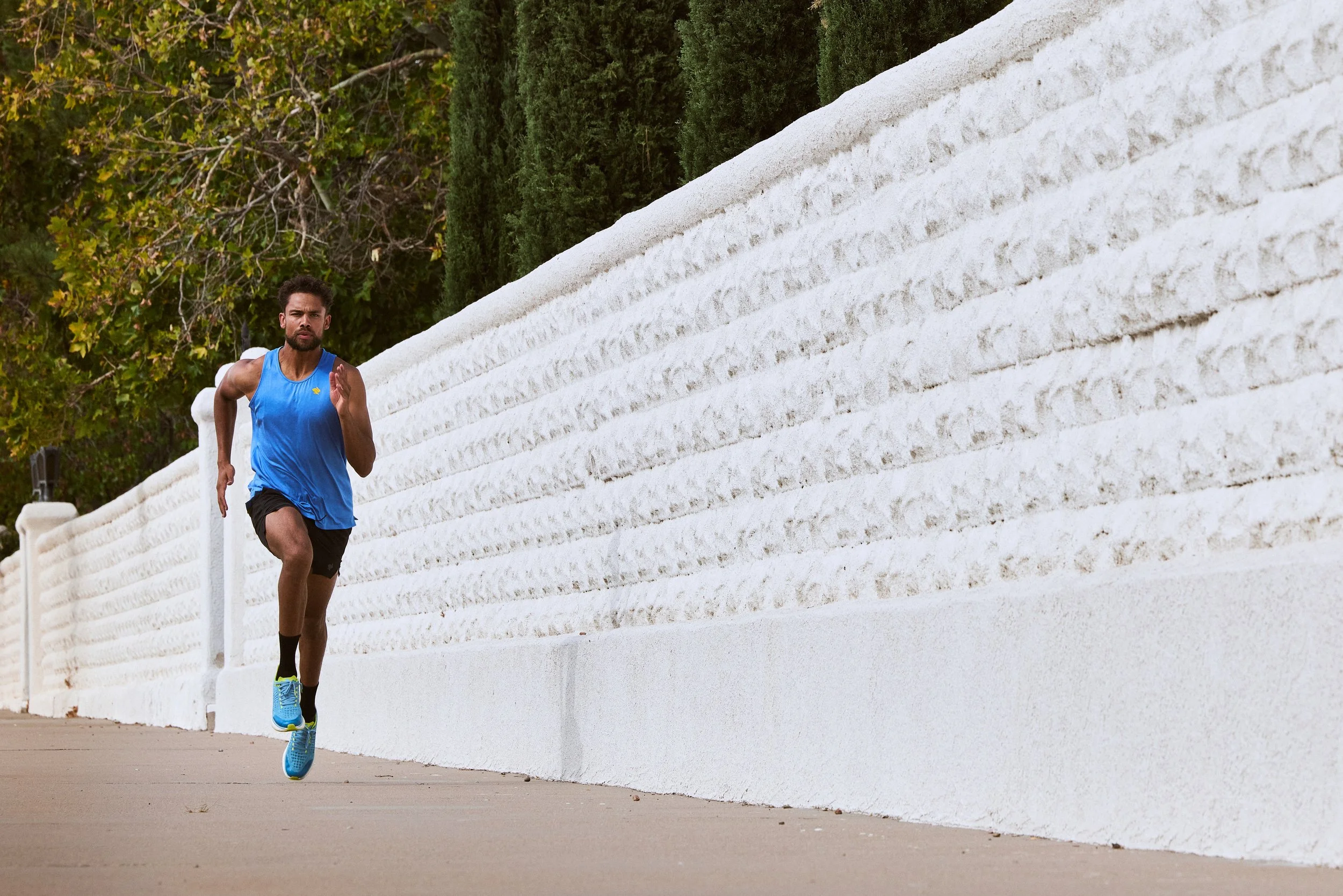 A man jogging along a white wall with green bushes behind him.