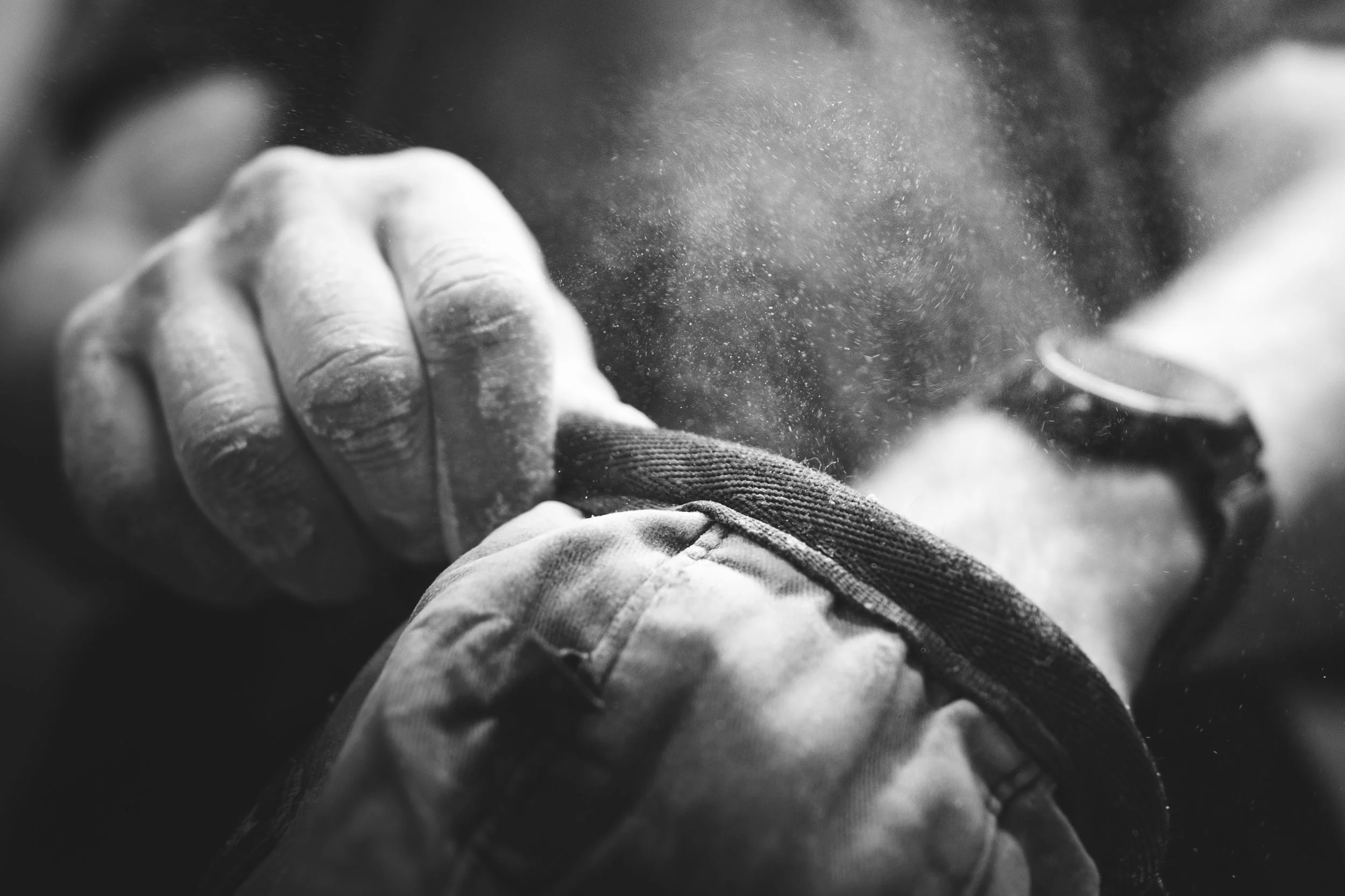 A black and white close-up image of a person’s hand holding a small object, with a blurred background. Dust or particles are visible in the air.