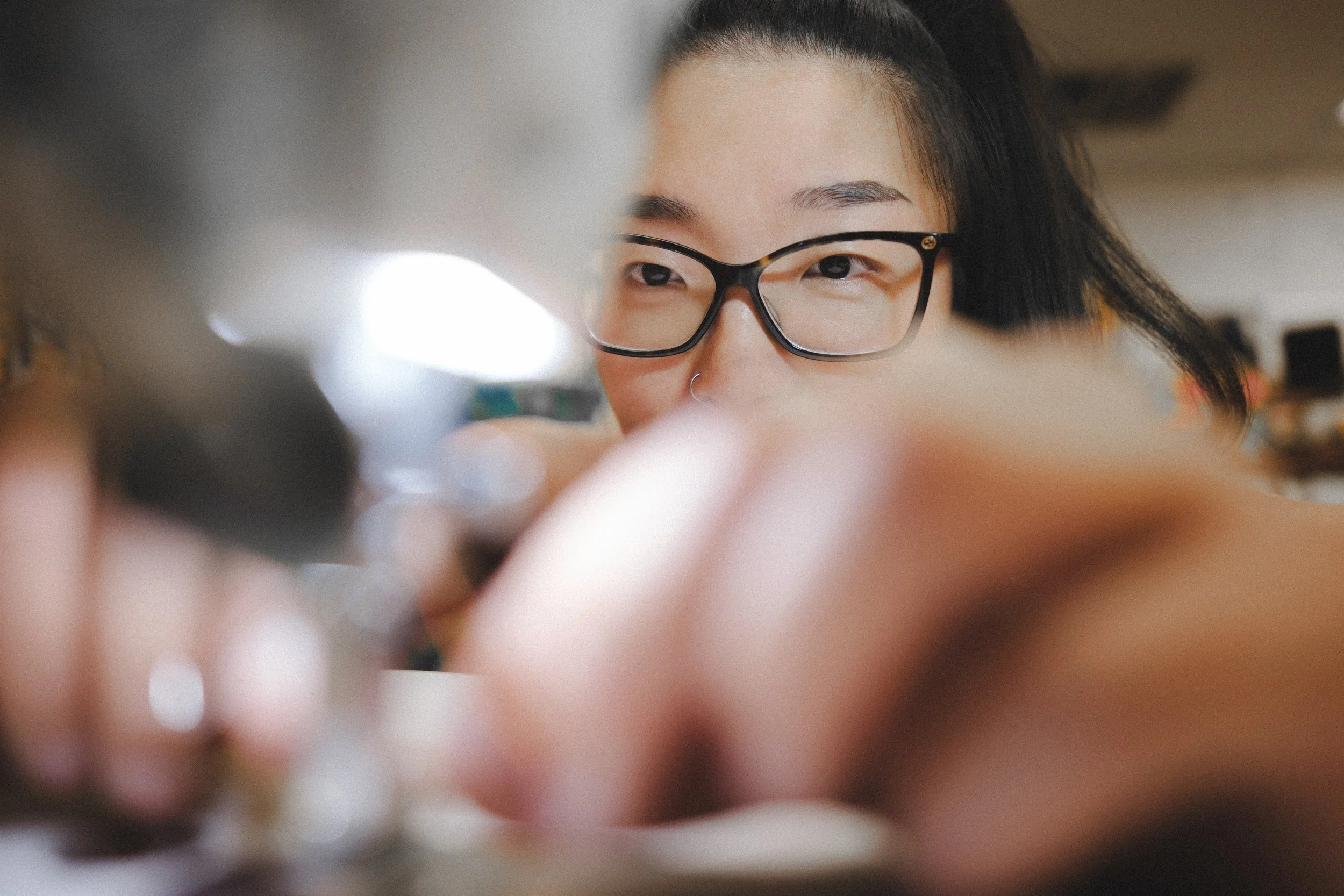 Close-up of a person with glasses, smiling, and looking at something, blurry foreground and background.